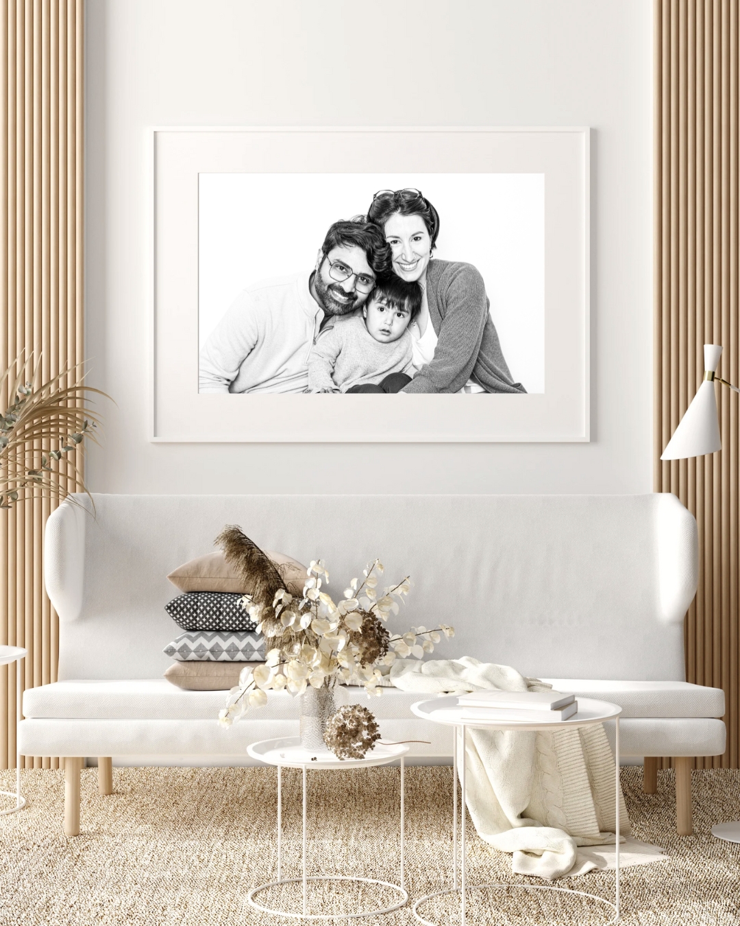 Black and white family portrait of three people smiling, hanging on a white wall above a white sofa in a modern living room.