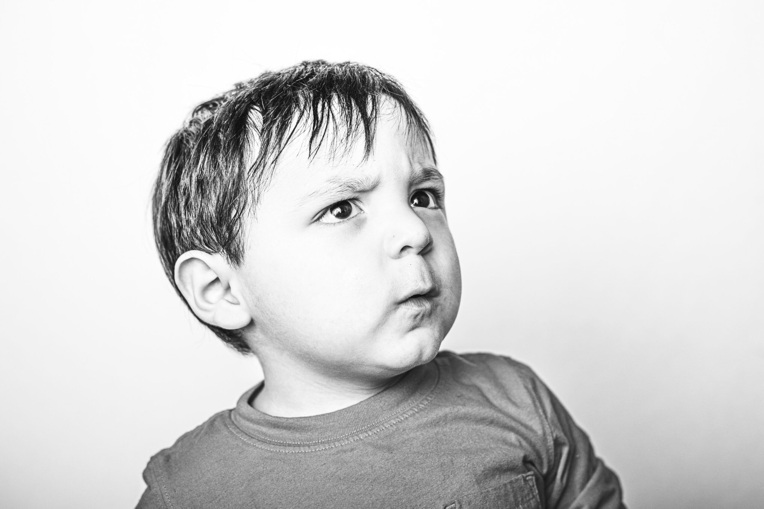 Child with short hair and a puzzled expression, wearing a T-shirt, looking to the side, black and white photo.
