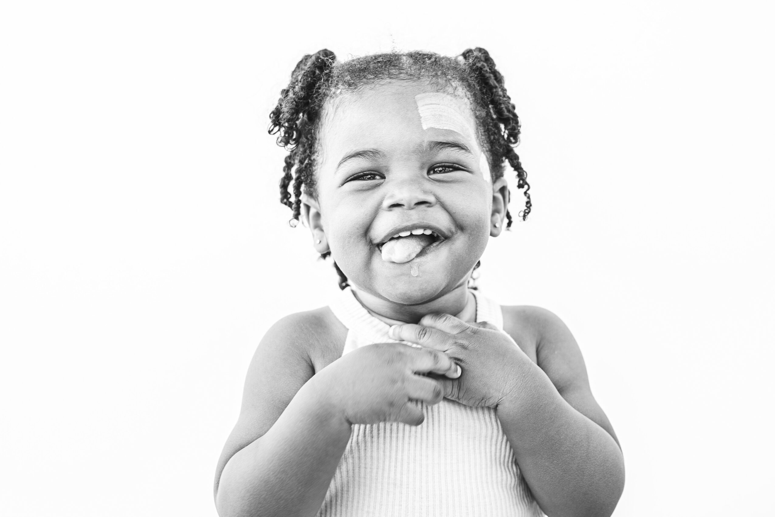 Young girl smiling with hands near her chest, wearing a sleeveless top, with curly hair styled in puffs.