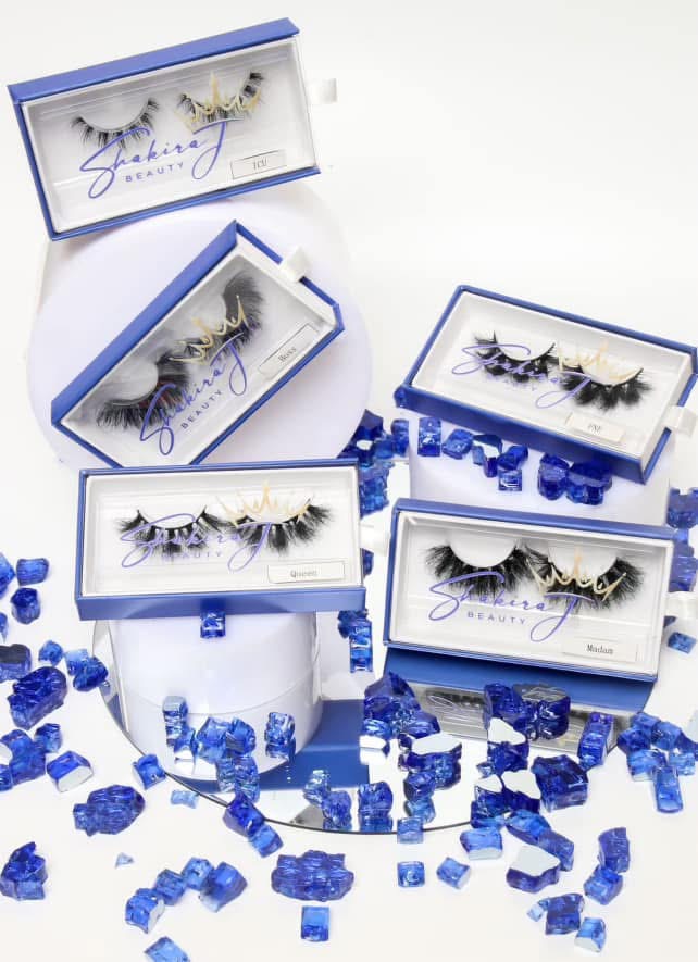 Five eyelash extension sets in boxes with blue decorations scattered around, on a white background.