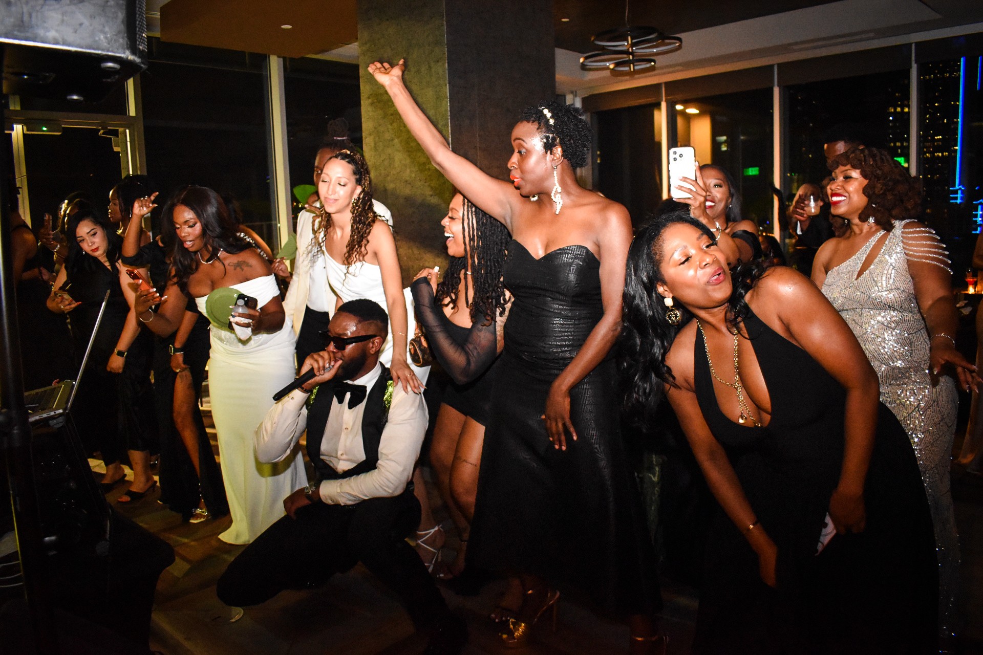 Group of people dancing and enjoying a party indoors, dressed in formal attire, with some raising hands and smiling.