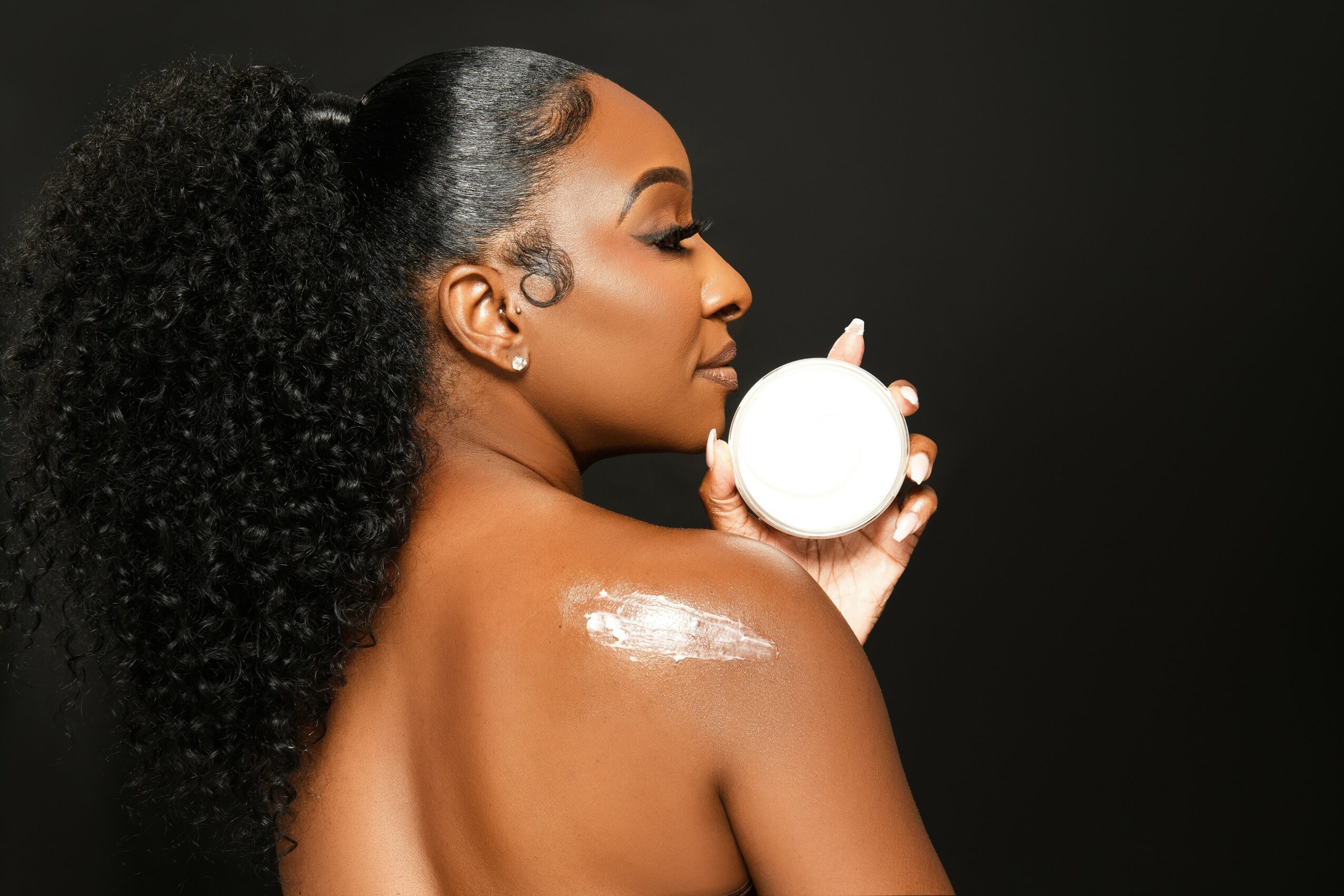 Profile of a woman with curly hair holding a round container, with a dark background.