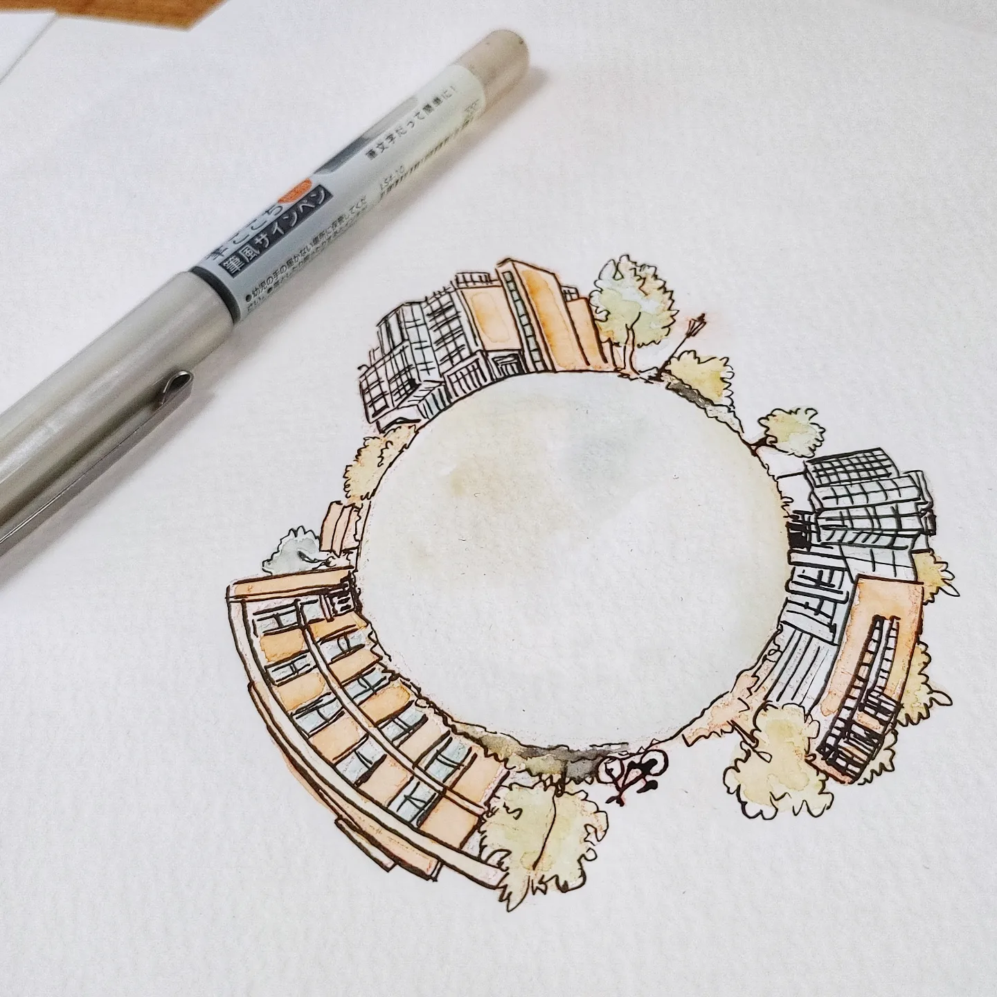 Circular illustration of buildings and trees on white paper with a gray marker nearby.