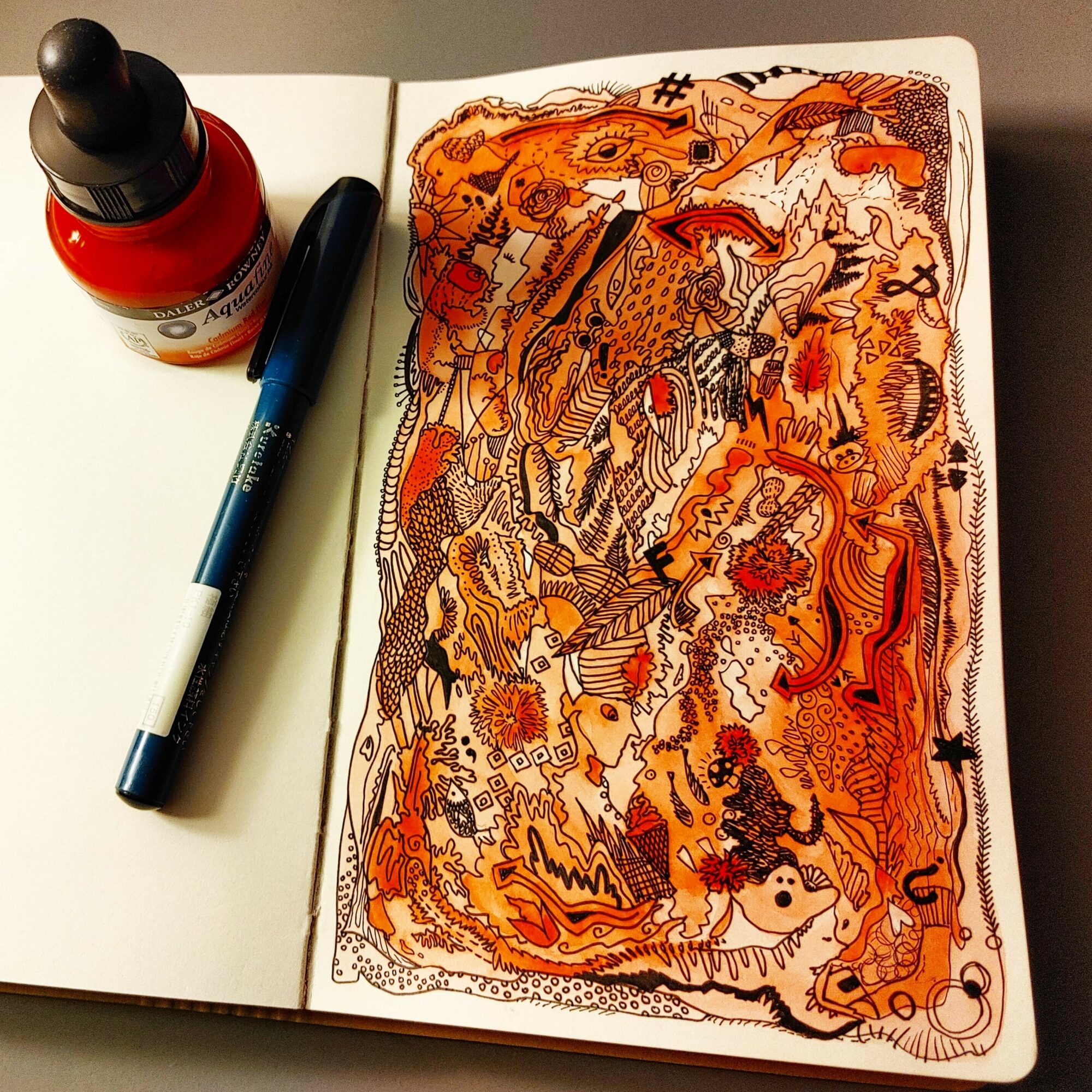 Open sketchbook with abstract, colorful drawing in orange, black, and red tones, accompanied by a black pen and red ink bottle.