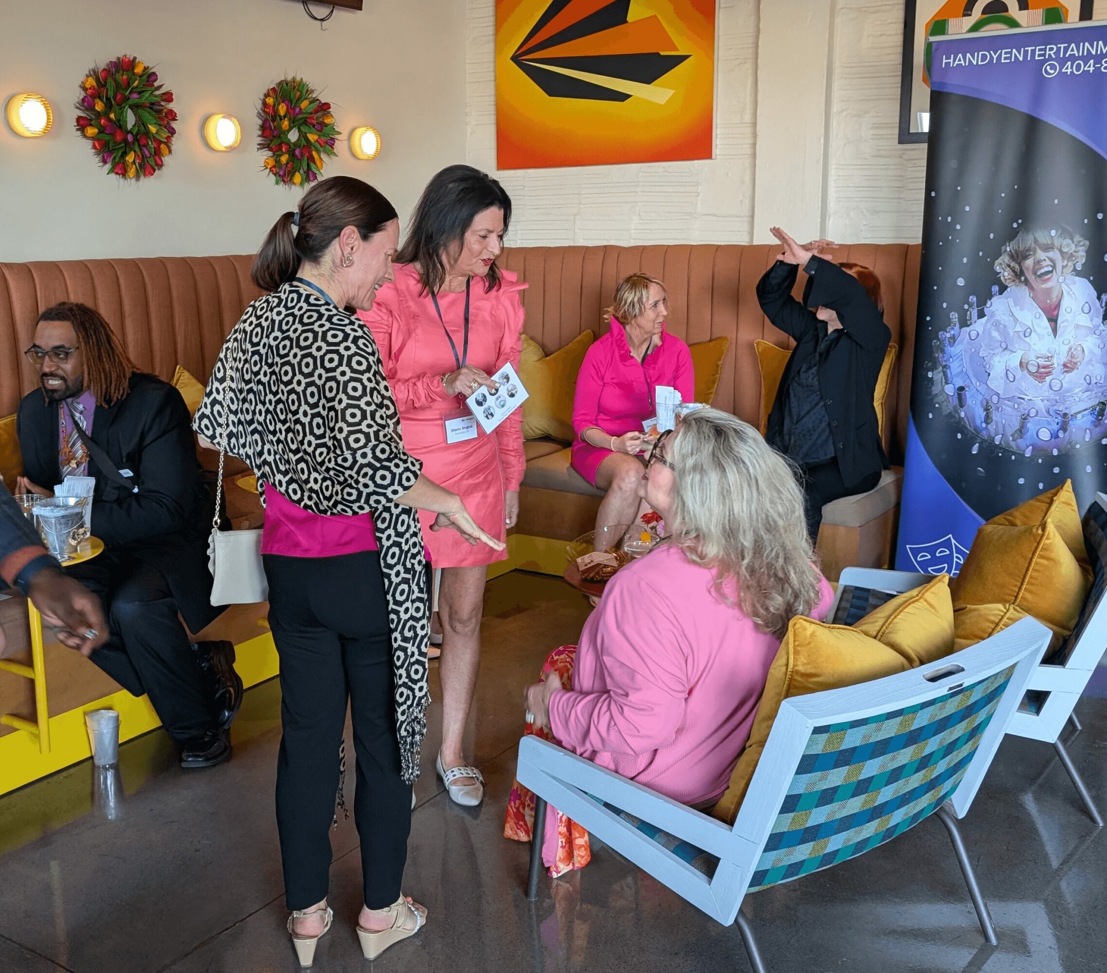 Group of people talking and sitting in a colorful indoor space with decorations and a banner.