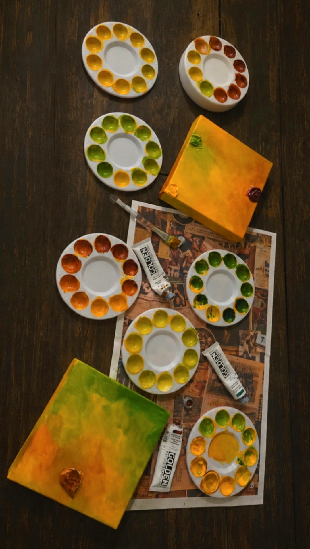 Paint palettes, a box, and newspapers on a dark wooden surface.