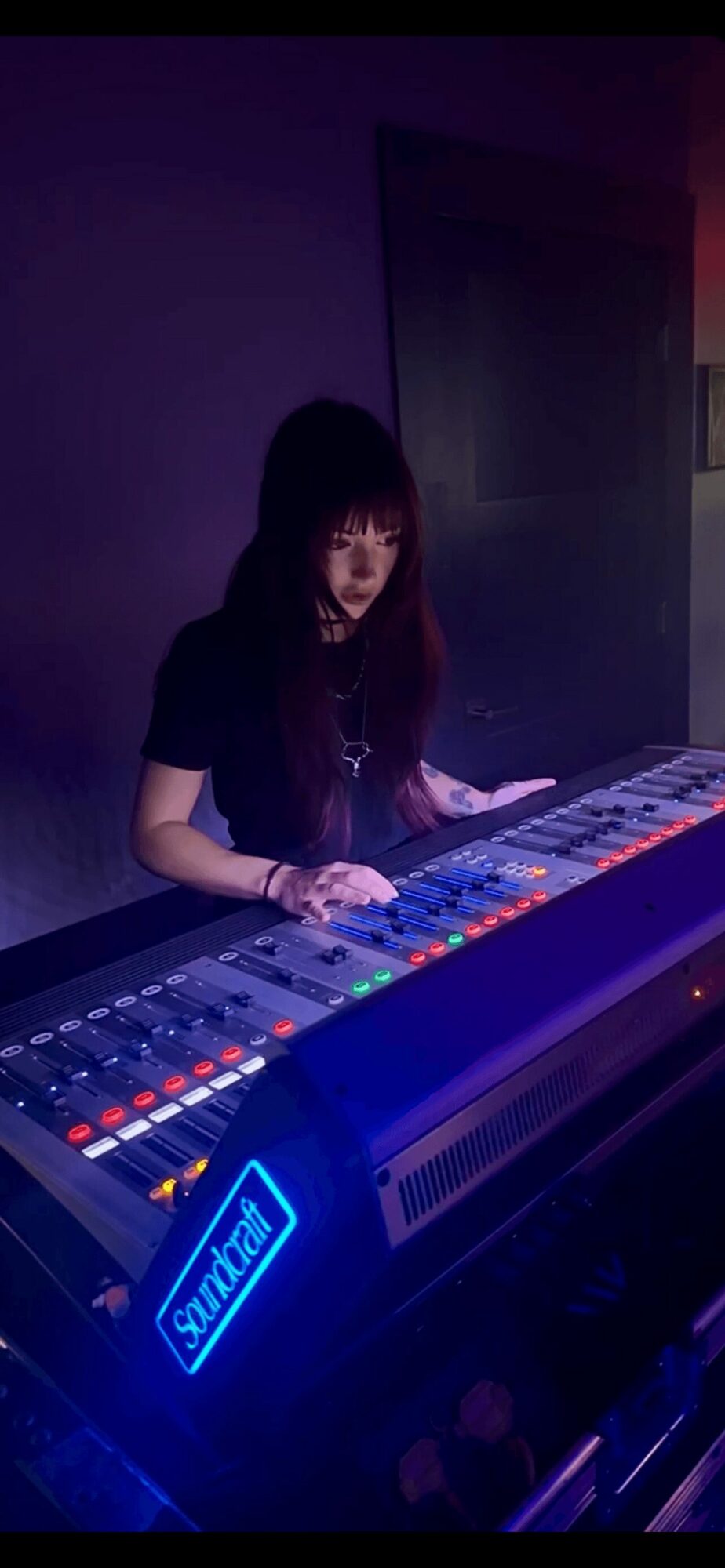 Person playing a digital piano with colorful lights, dark background, and a blue illuminated sign.