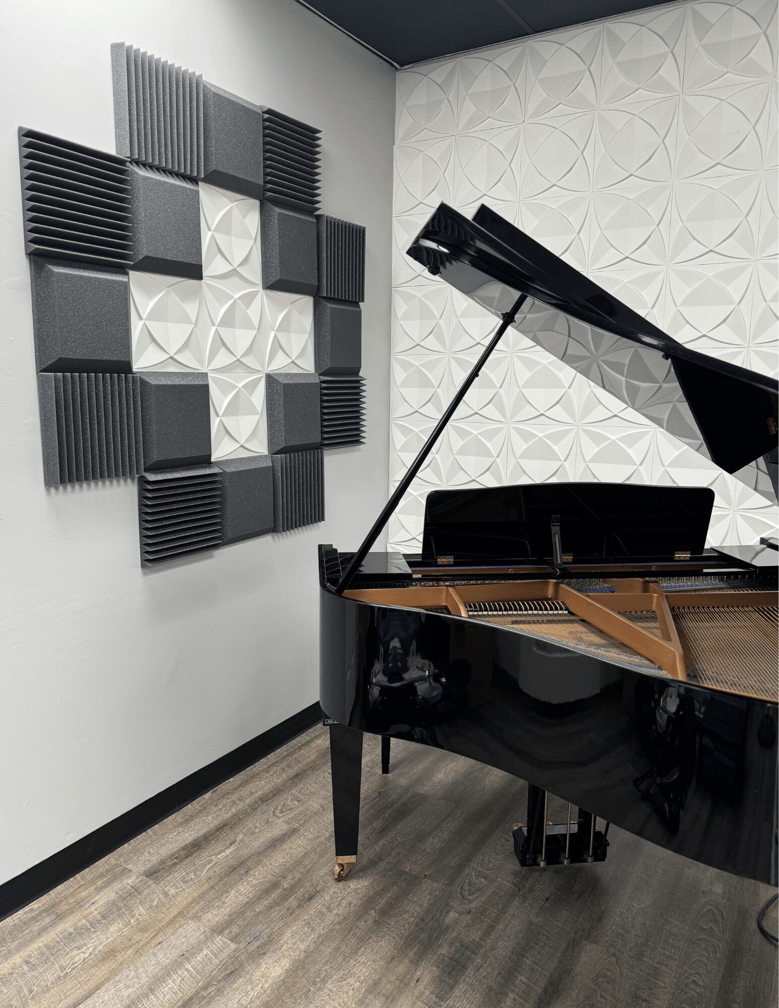 Grand piano in a music room with acoustic foam panels on the wall, wooden floor, and patterned wall background.