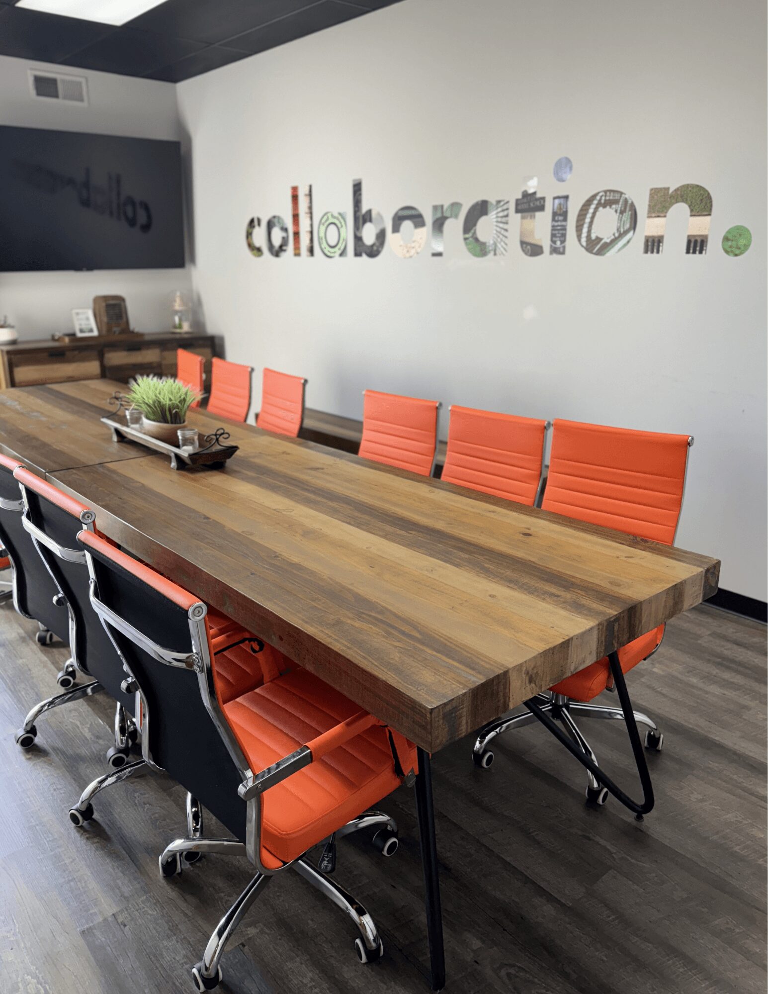 Conference room with a long wooden table and orange chairs, wall with colorful letters spelling 'collaboration'.