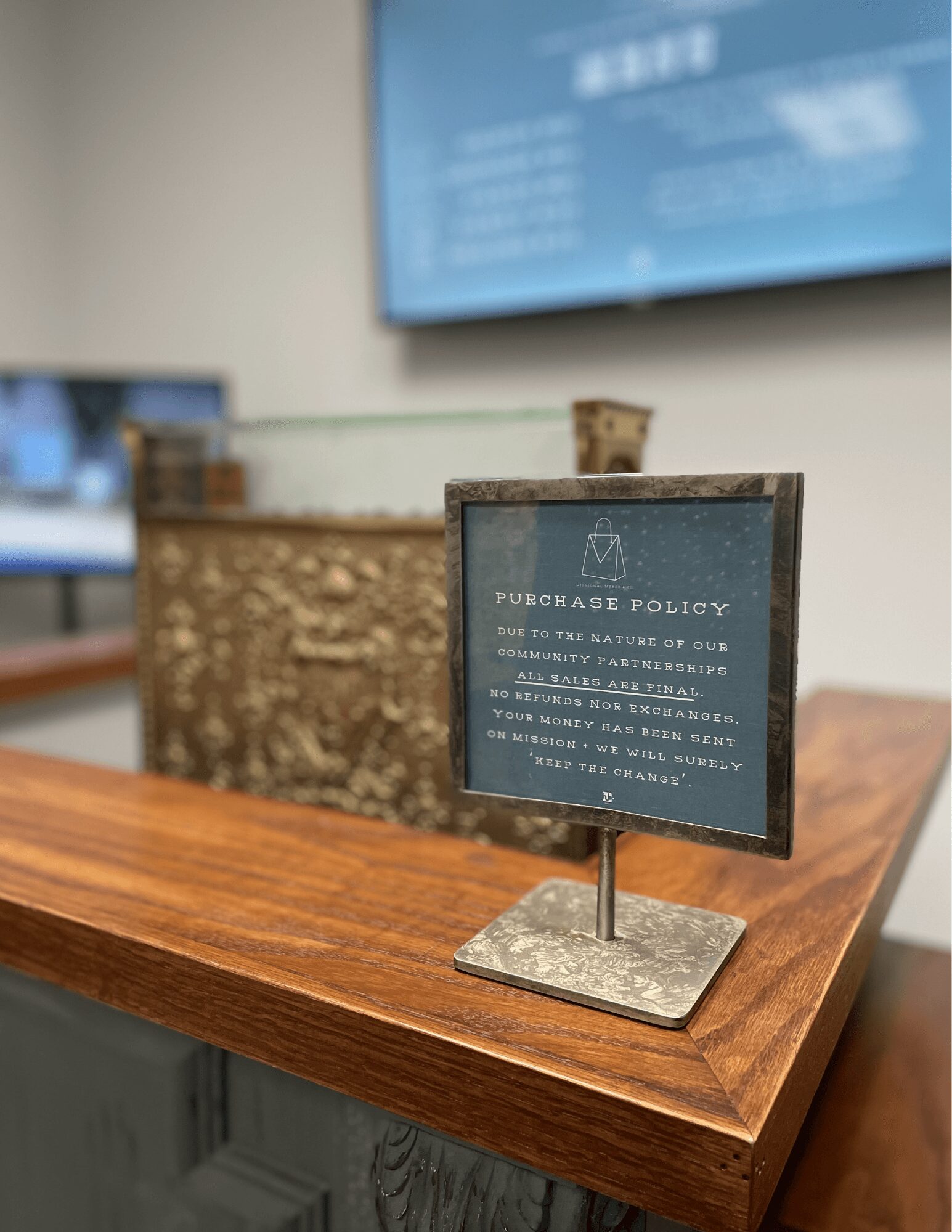 Small sign on a wooden table displays purchase policy information, with a blurred background of a reception area or office.