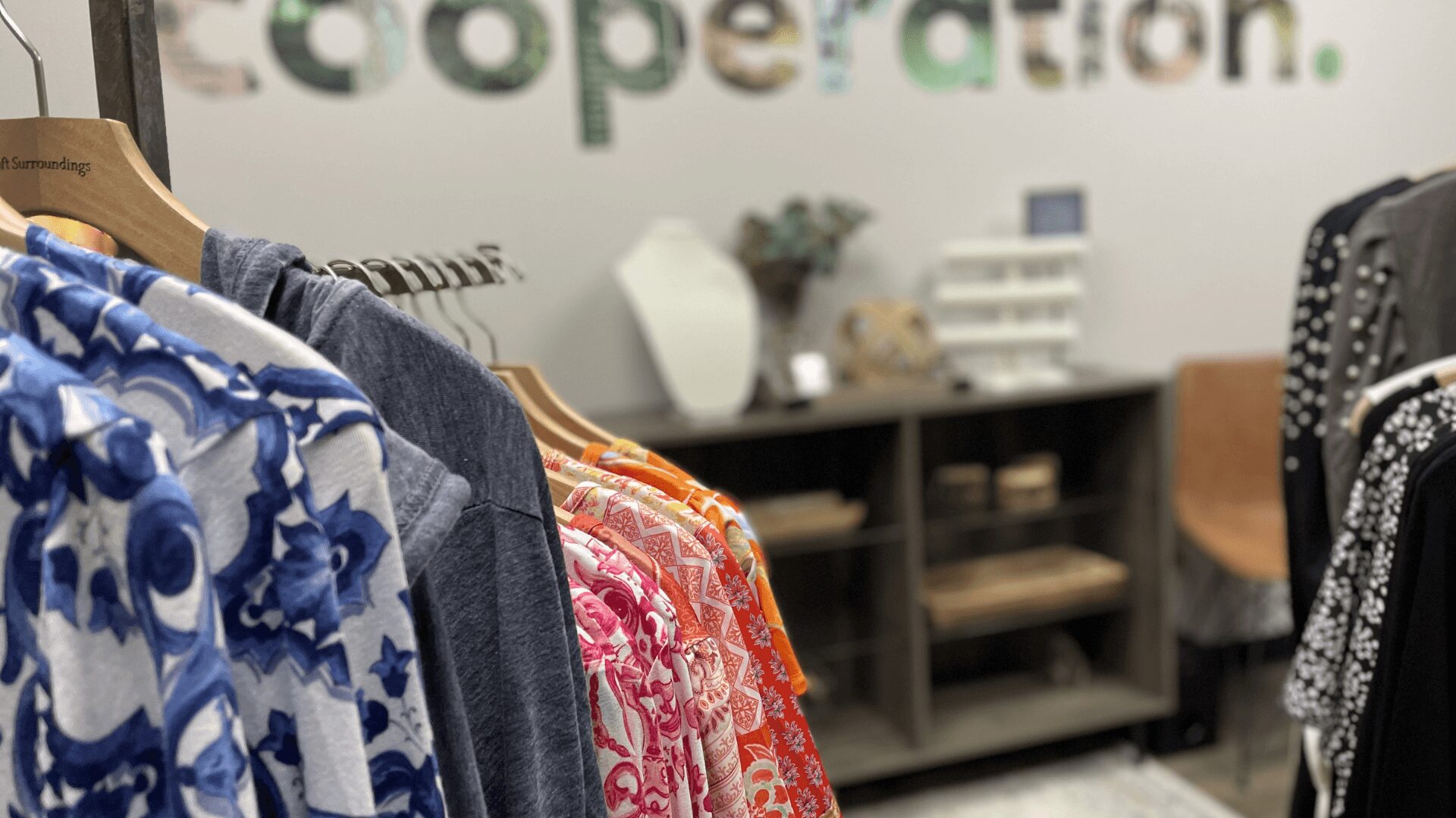 Clothing rack with colorful garments in a store, with a blurred background of a wall and shelves.