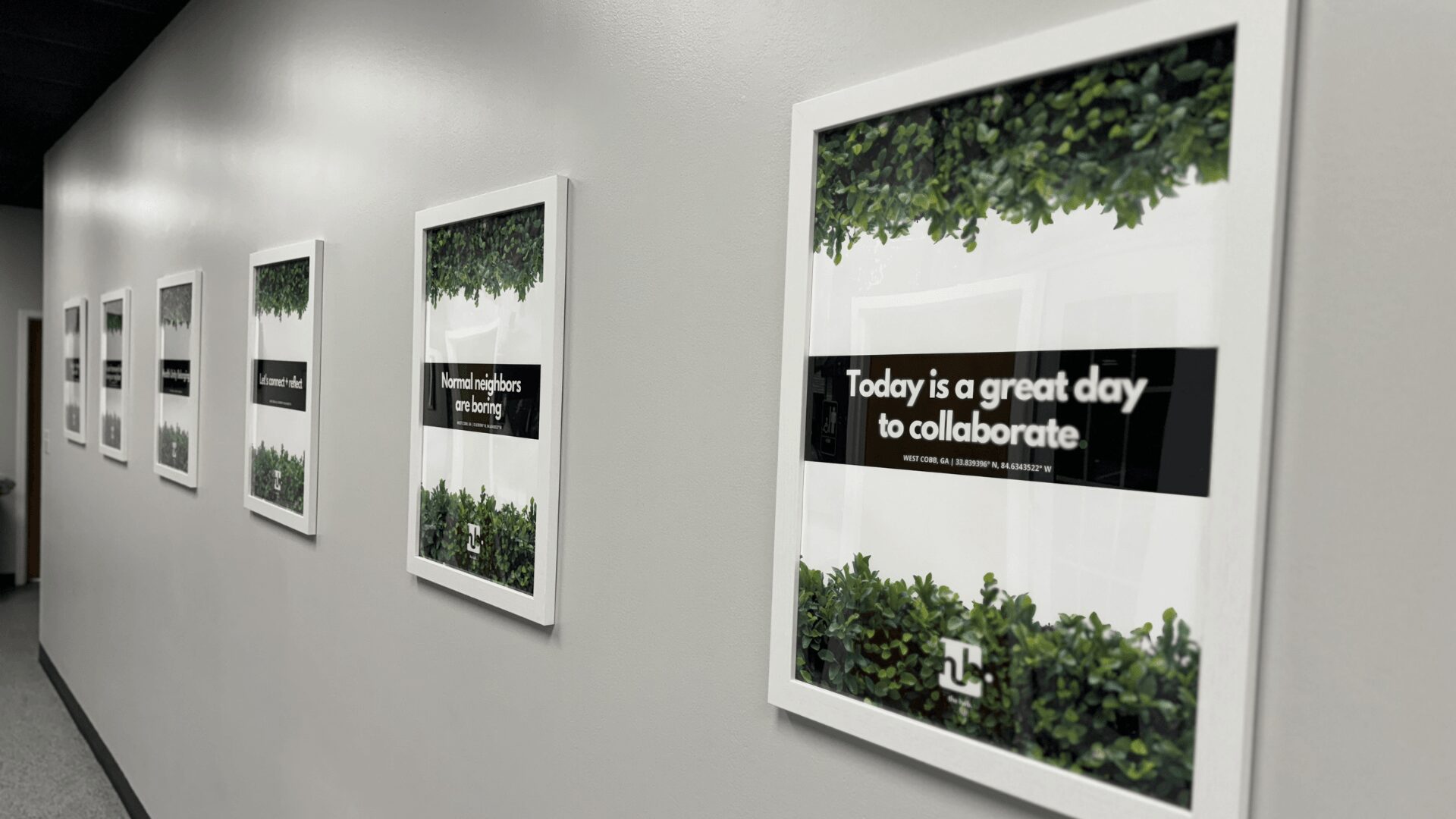 Gallery wall with framed posters featuring greenery and motivational messages, arranged in a row on a white wall.