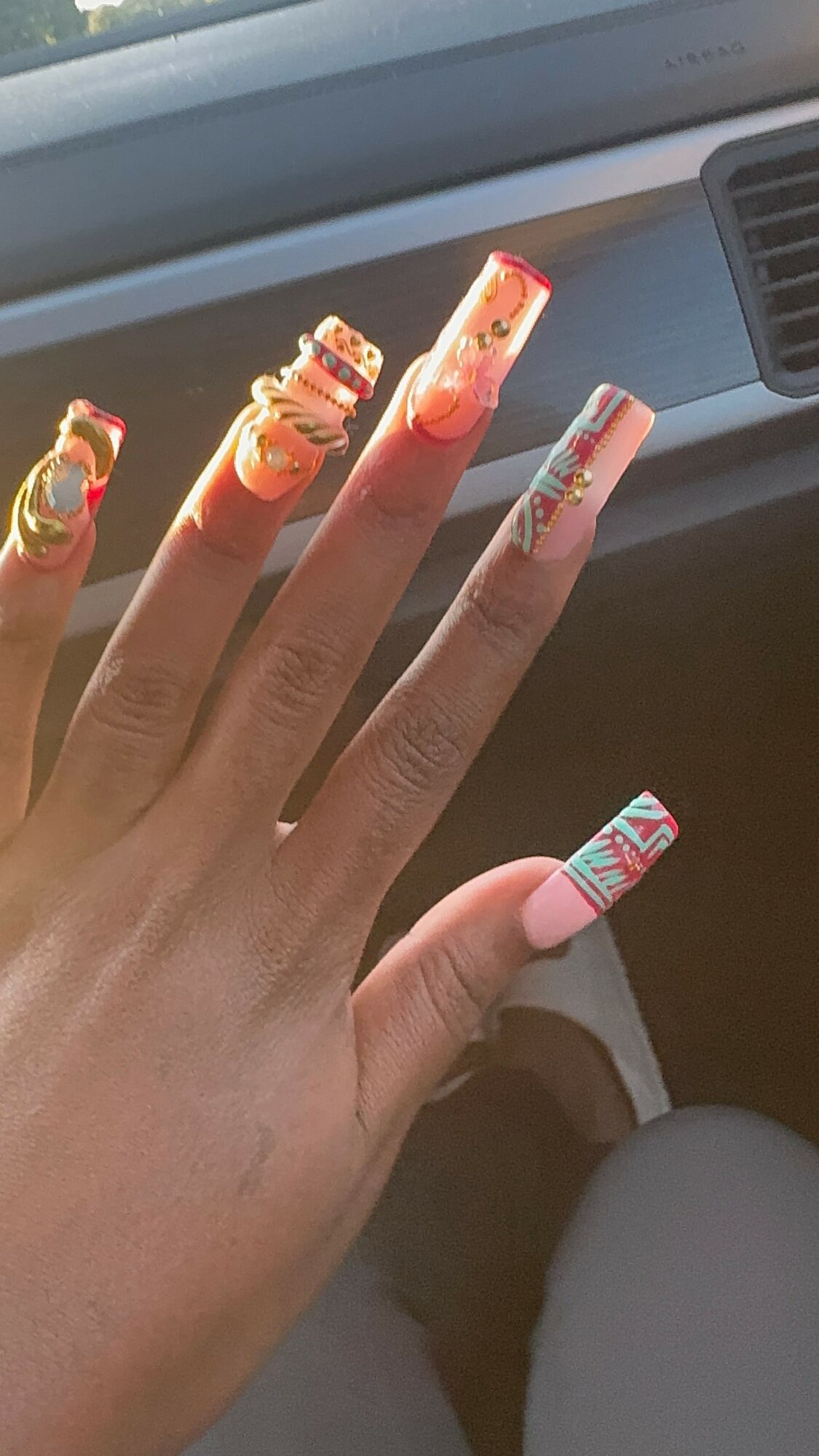 Hand with decorated long nails, each with colorful, intricate designs, near a car window and dashboard.