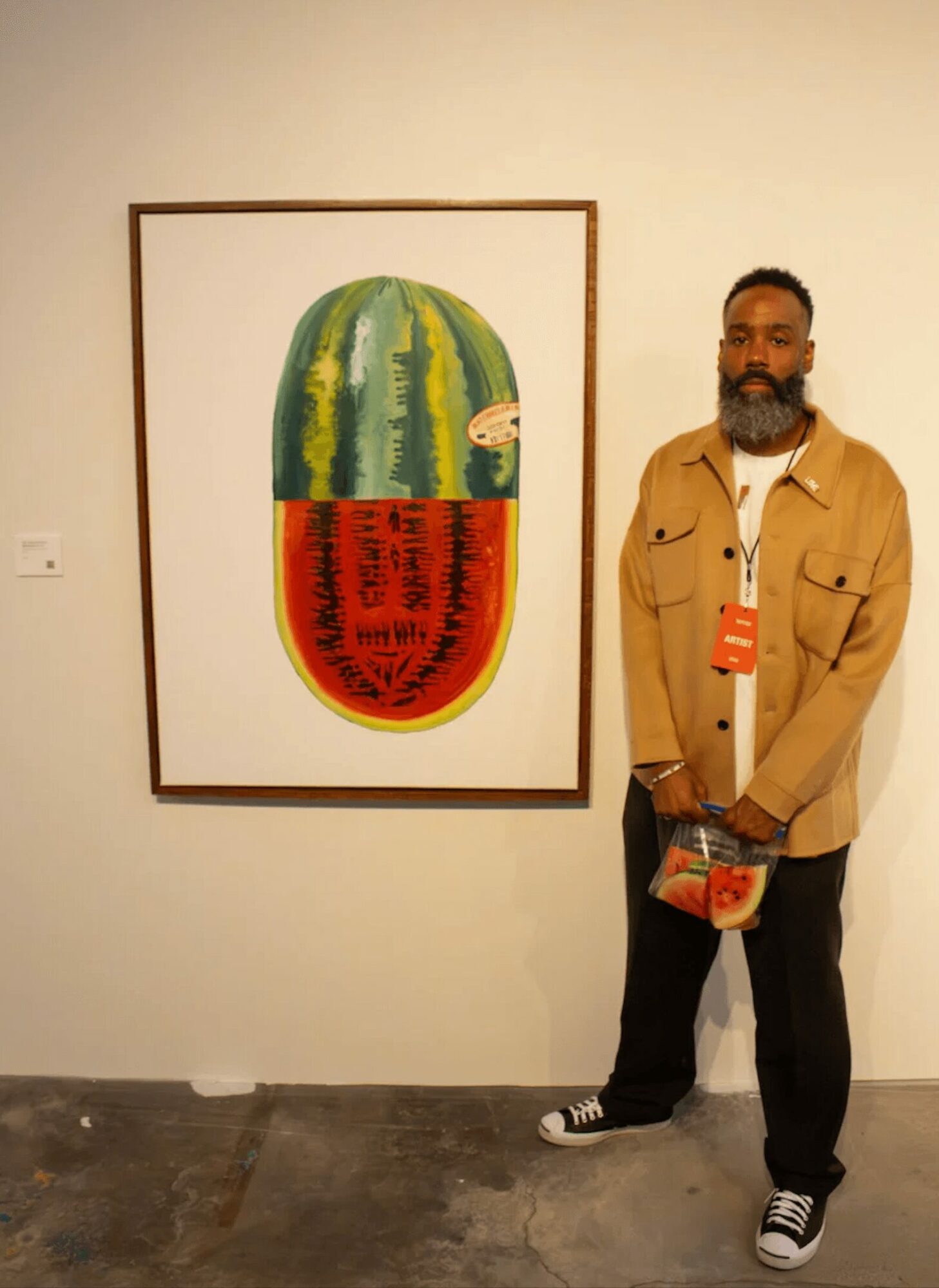 Man with a beard and glasses stands next to a colorful abstract painting on a white wall.