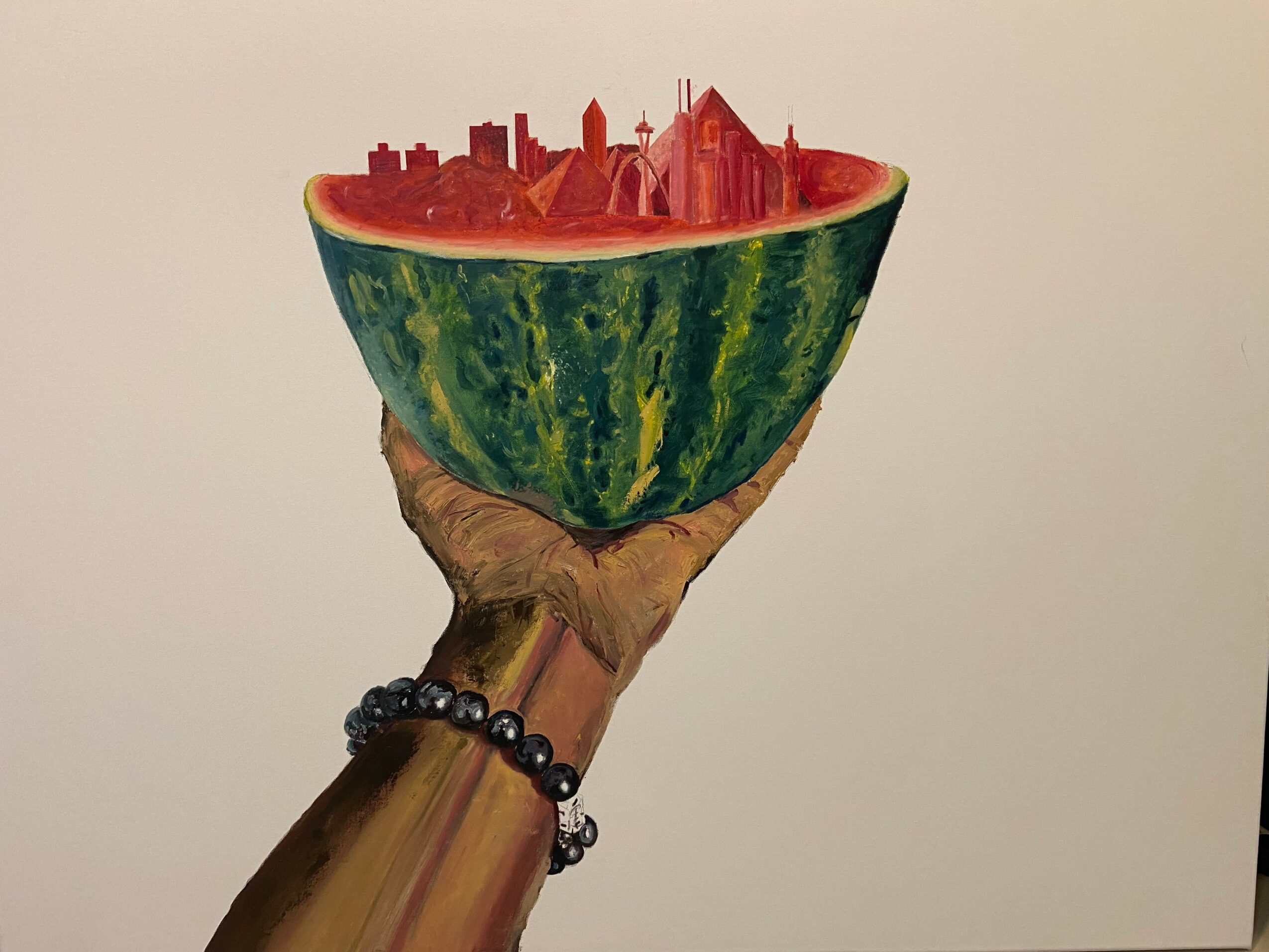 A hand holding a watermelon half with a cityscape inside, including buildings and skyscrapers, on a plain background.