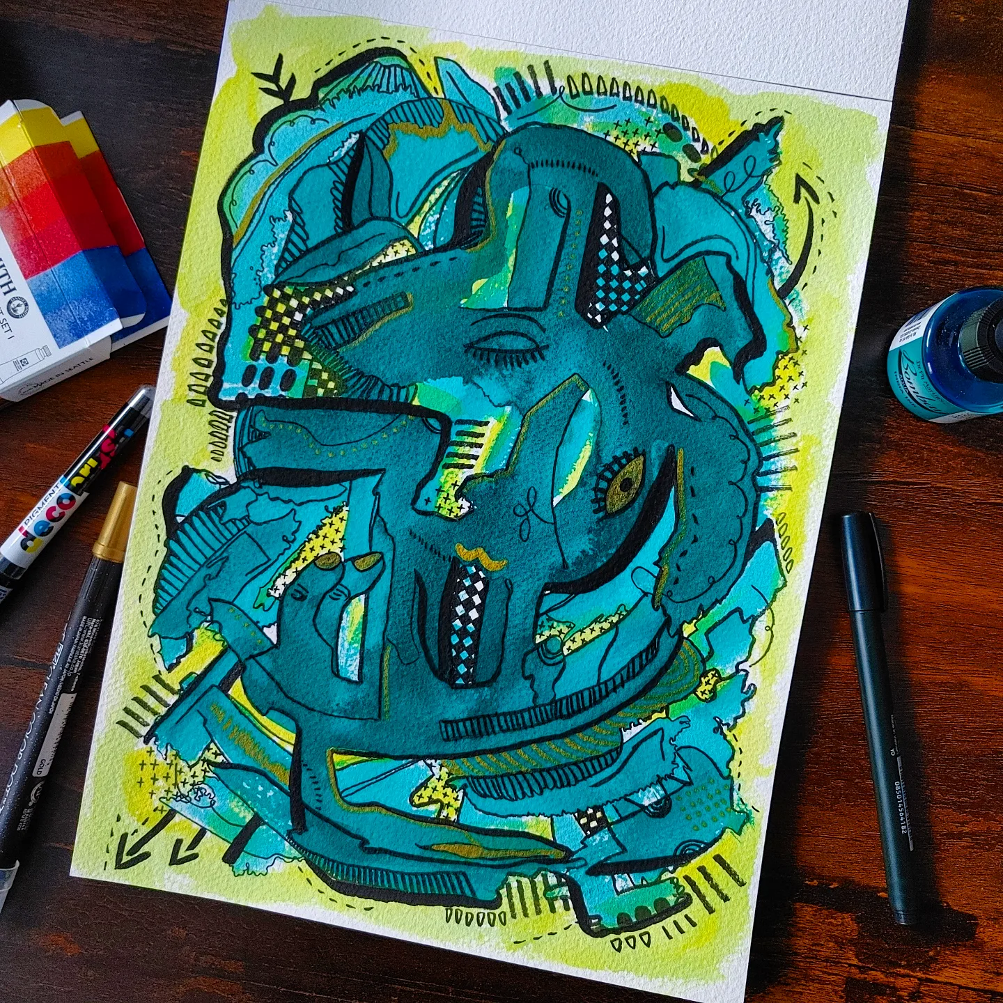 Colorful abstract graffiti-style artwork with blue, green, and black shapes on white paper, surrounded by art supplies.
