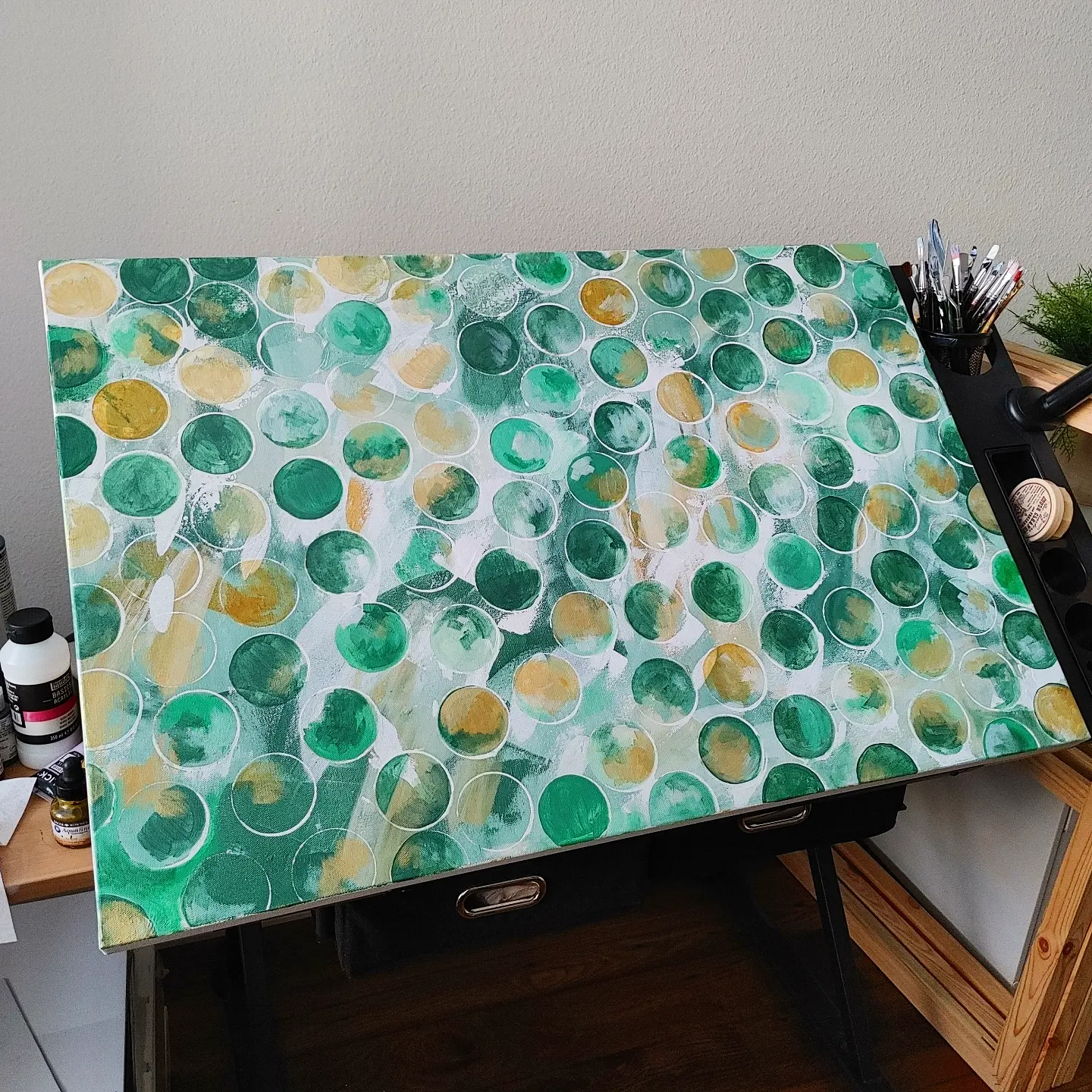 Table with a colorful abstract pattern of green, yellow, and white circles, surrounded by art supplies and a plant.
