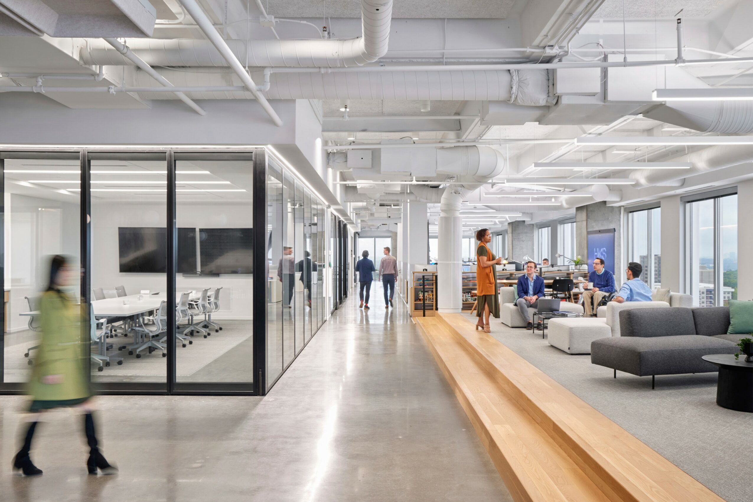 Modern office space with glass-walled meeting rooms, open seating area, and large windows with city view.