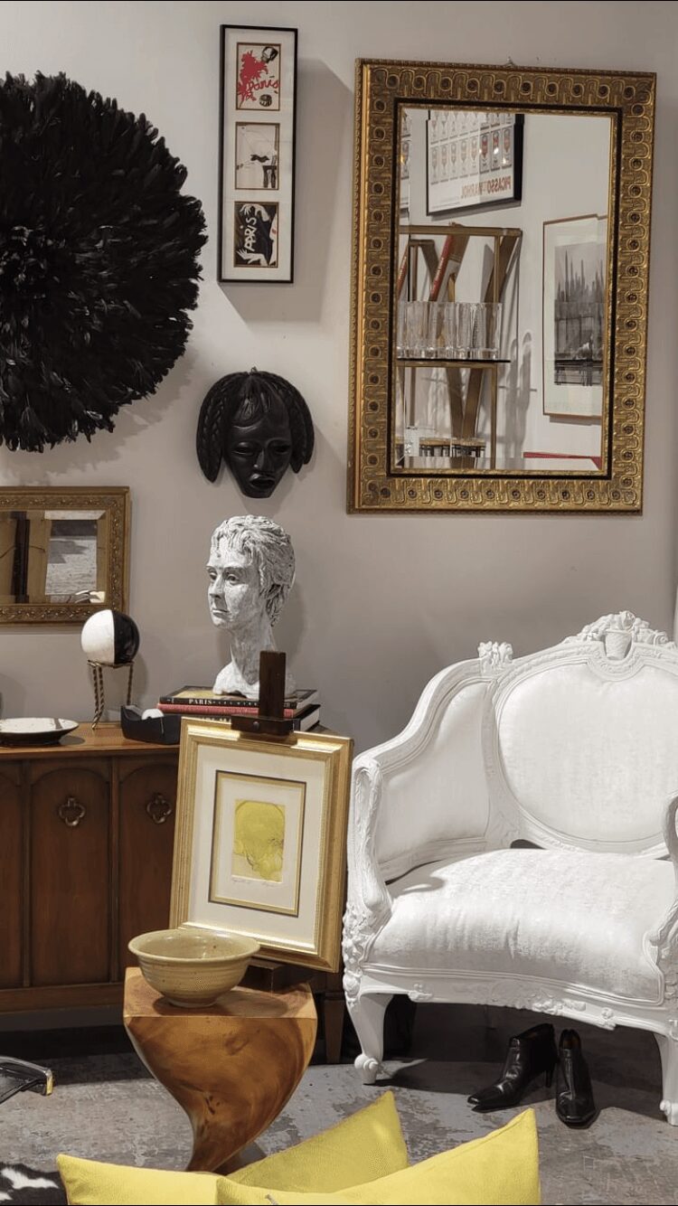 Living room wall with framed art, mirror, and decorative masks, white sofa, wooden cabinet, and various decorative items.
