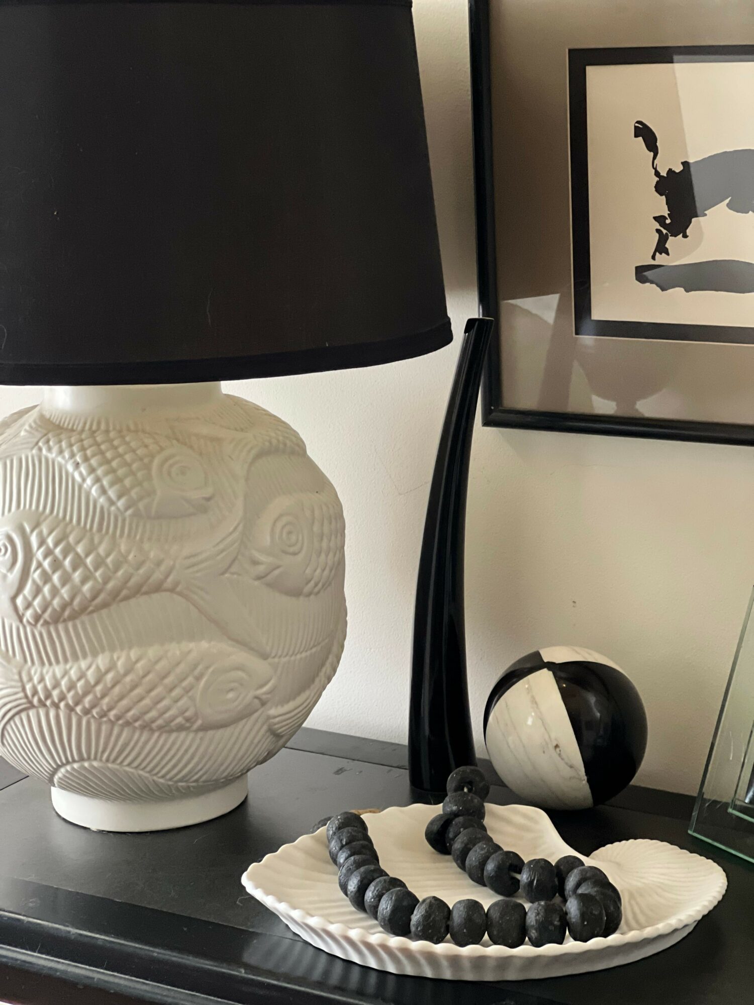 Decorative carved white sculpture of a snake on a black base, with a black and white spherical object and a beaded necklace on a white plate.