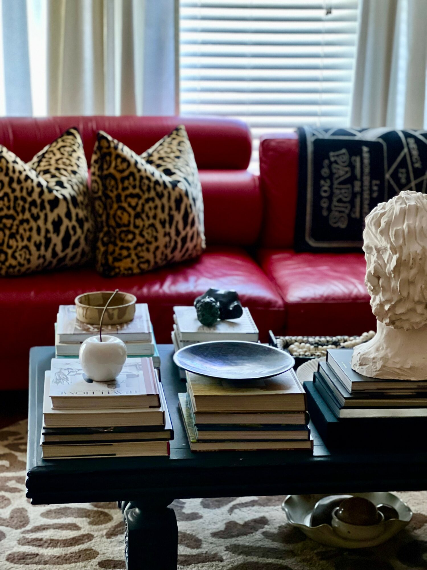 Living room with red sofa, leopard print pillows, and a coffee table with books, a bust sculpture, and decorative items.