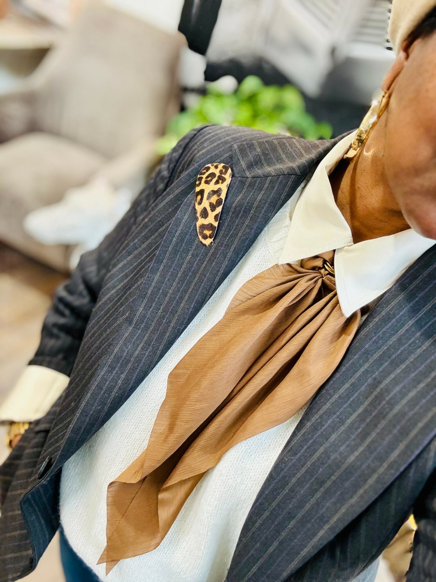 Close-up of a person wearing a pinstripe suit with a leopard-print brooch and a brown scarf tied around the neck.