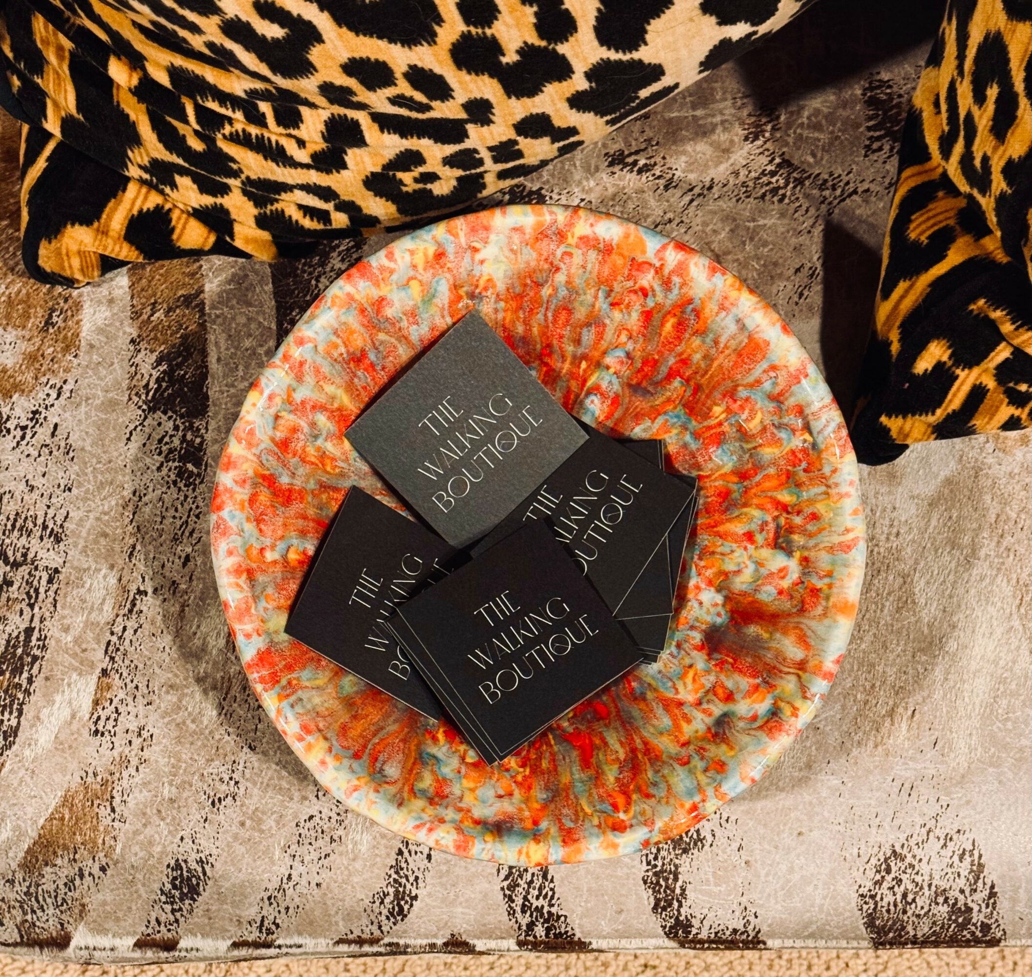Three black boxes labeled 'The Unique Boutique' on a colorful, textured round surface, with leopard print fabric in background.