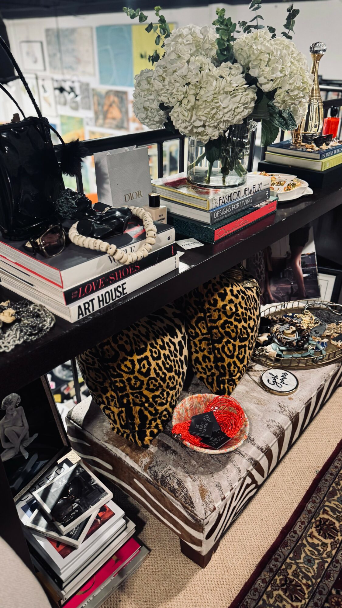 Decorative table with white flowers, books, and leopard print chairs, with various accessories and a patterned cushion.