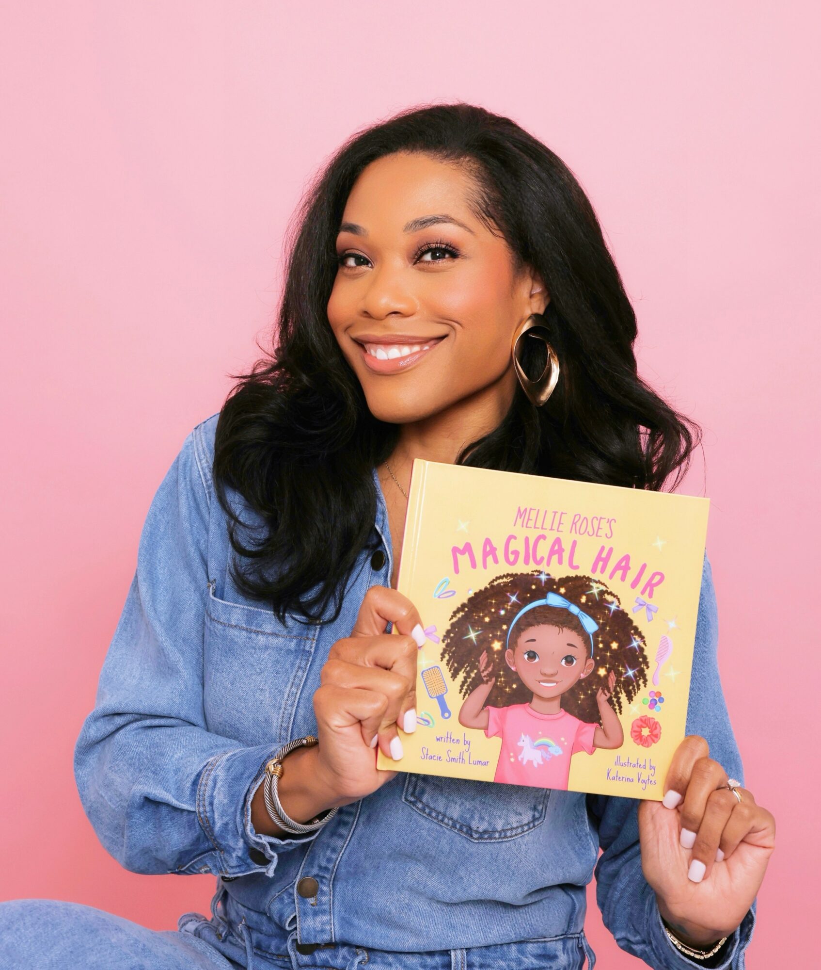 Smiling woman holding a children's book titled 'Magical Hair' against pink background.