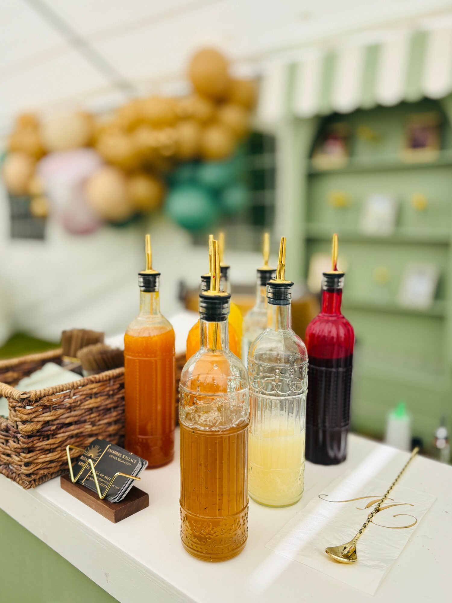 Five bottles with liquid, some with black caps, on a white surface, with a basket and store shelves in background.
