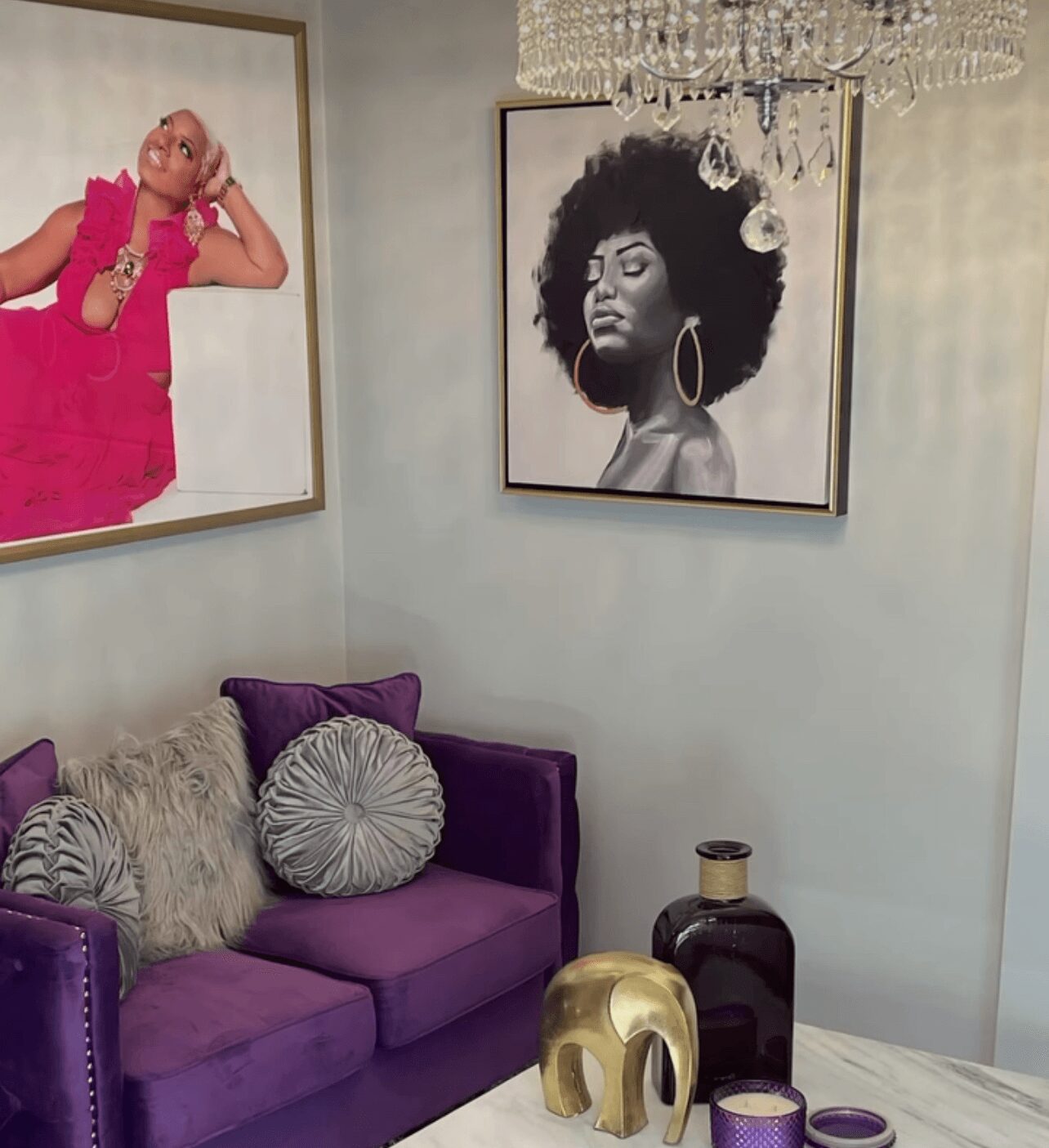 Living room corner with purple sofa, decorative pillows, black and gold vases, and framed black-and-white portraits on the wall.