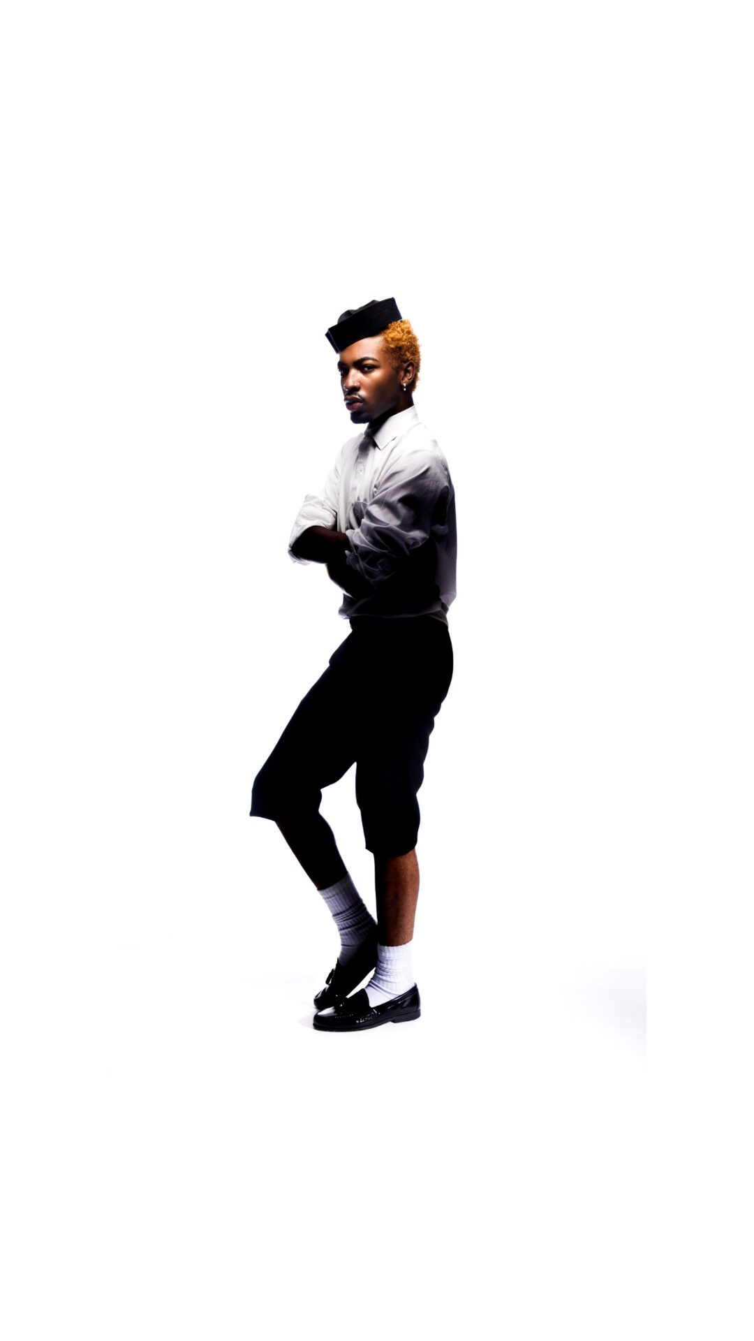 Person standing with arms crossed, wearing a light shirt and dark pants, against a white background.