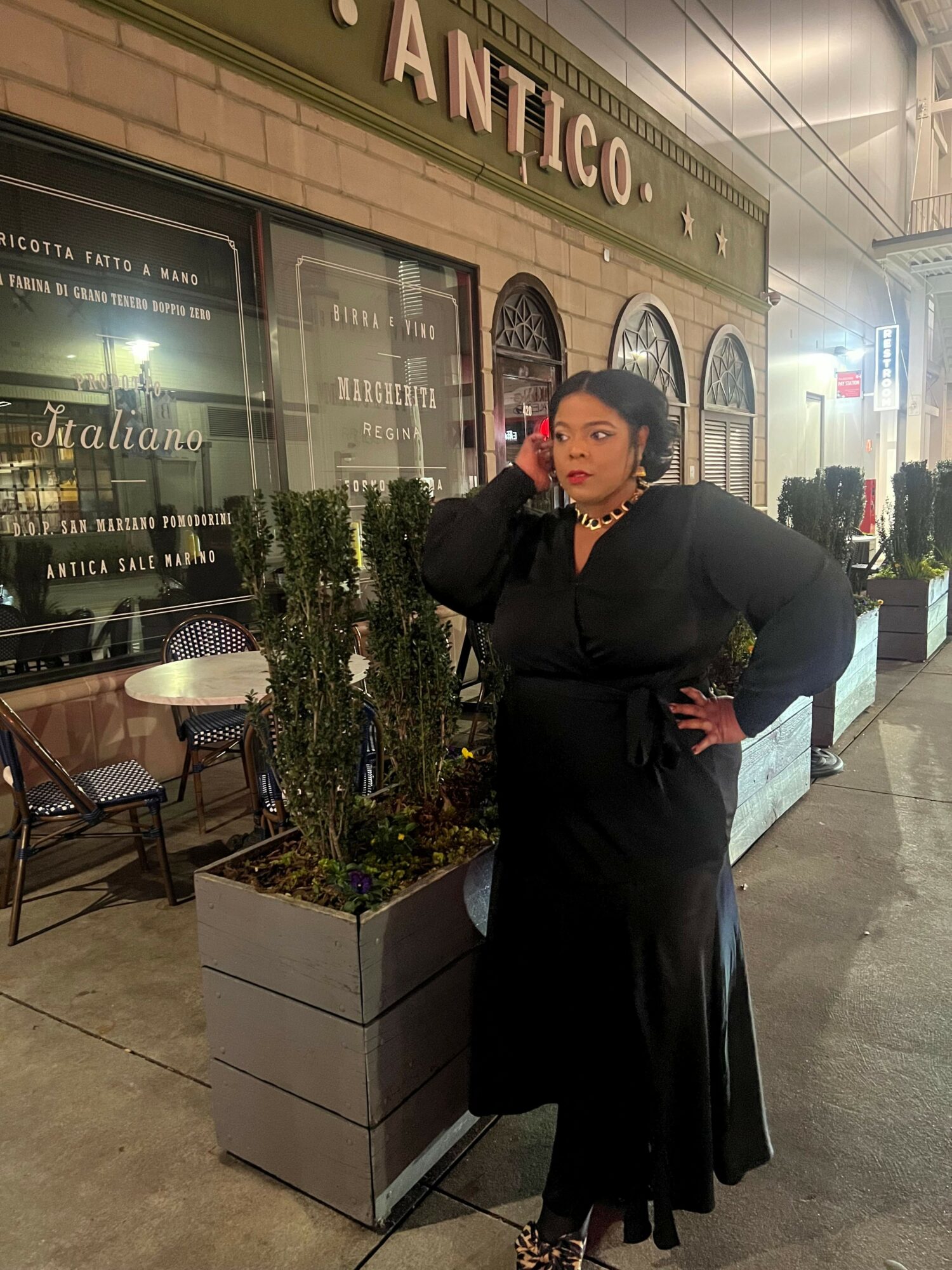 Person in black coat standing outside near a building with a sign reading 'ANTICO' and a window display.