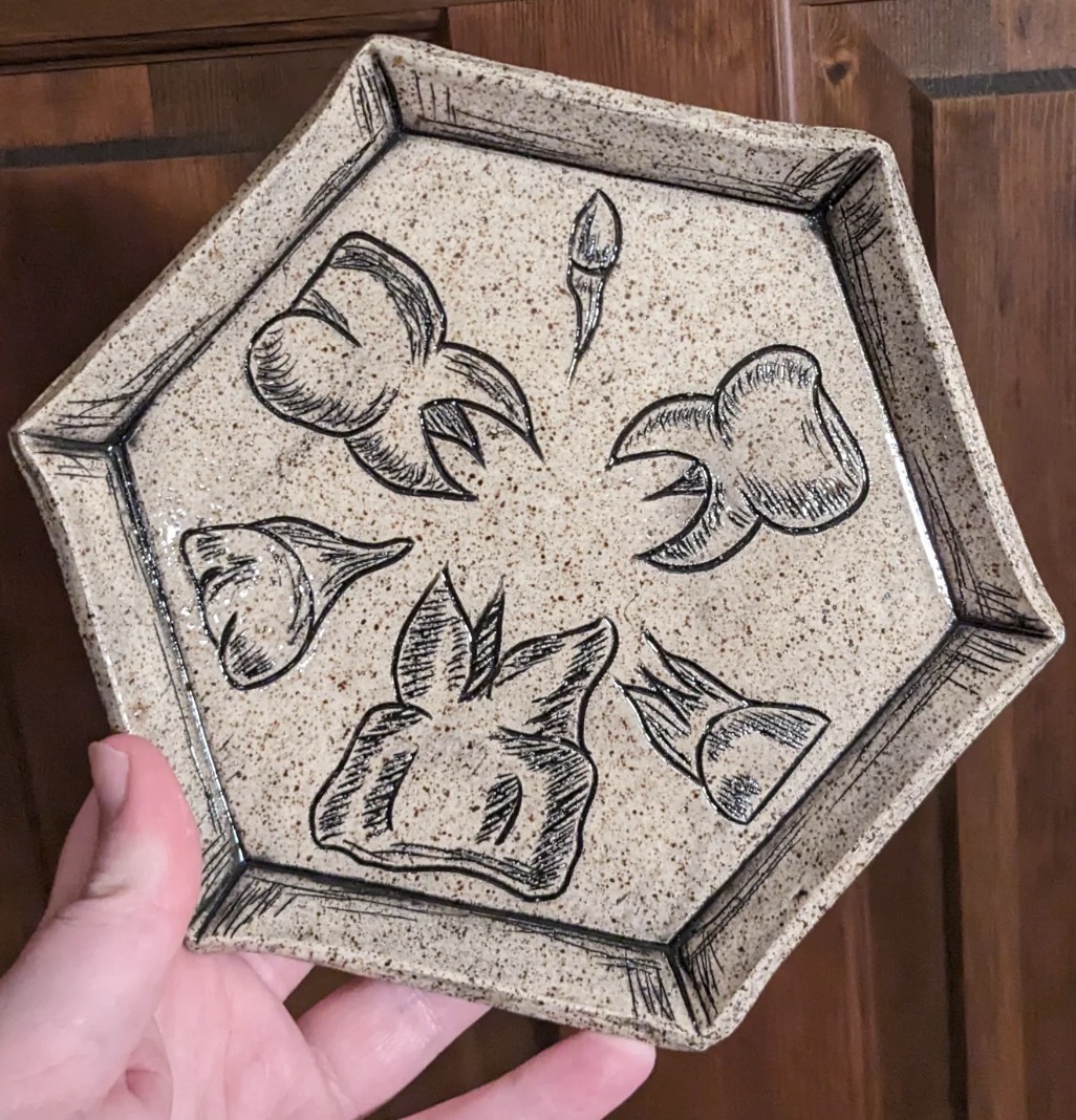 Hexagonal tray with floral and animal designs, held by a person's hand, against a wooden background.