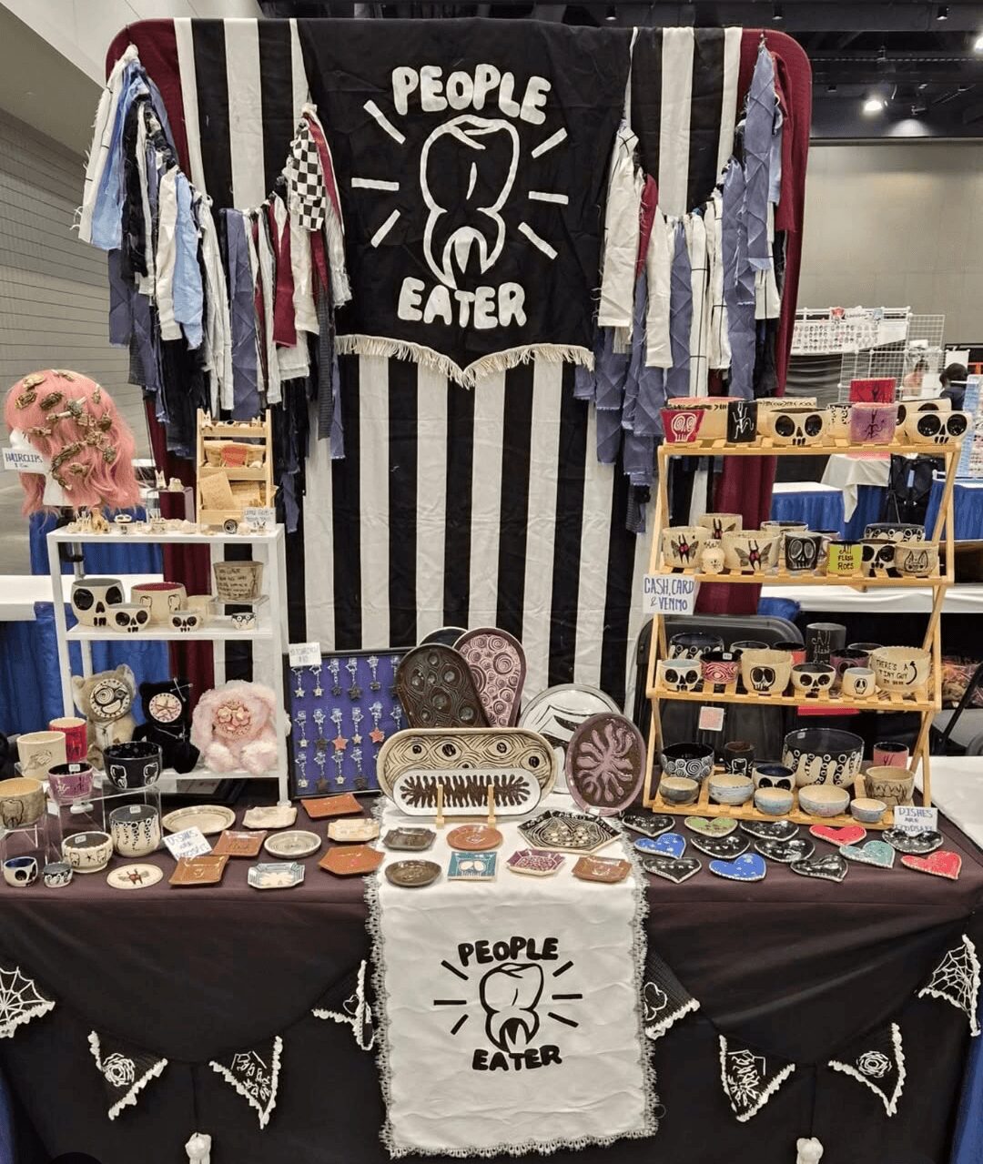 Display of clothing, accessories, and decorative items with a black and white striped backdrop and a sign reading 'People Eater'.