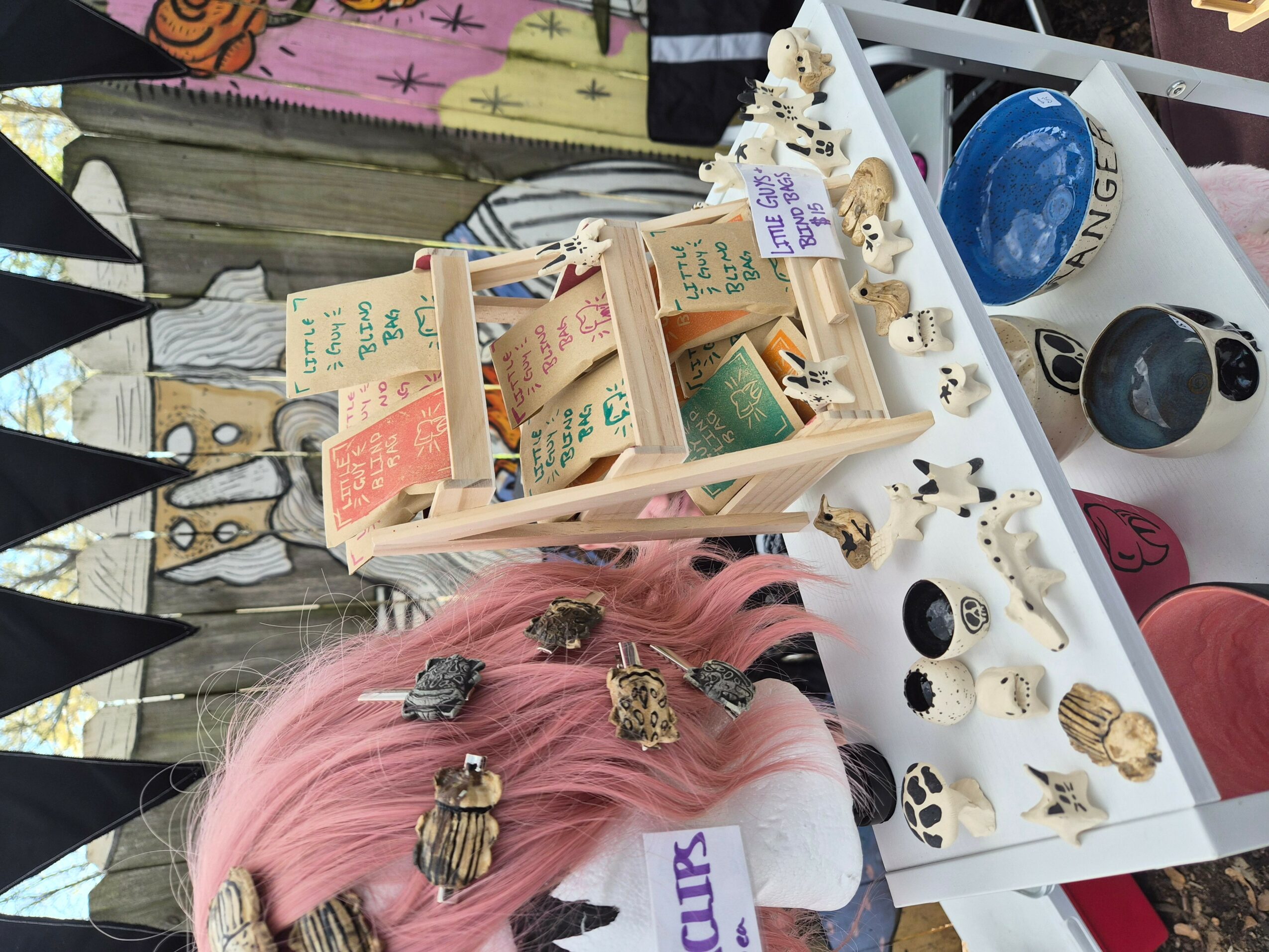 Pink-haired person with bees on head, display of small figurines and collectibles on table, and various items in background.