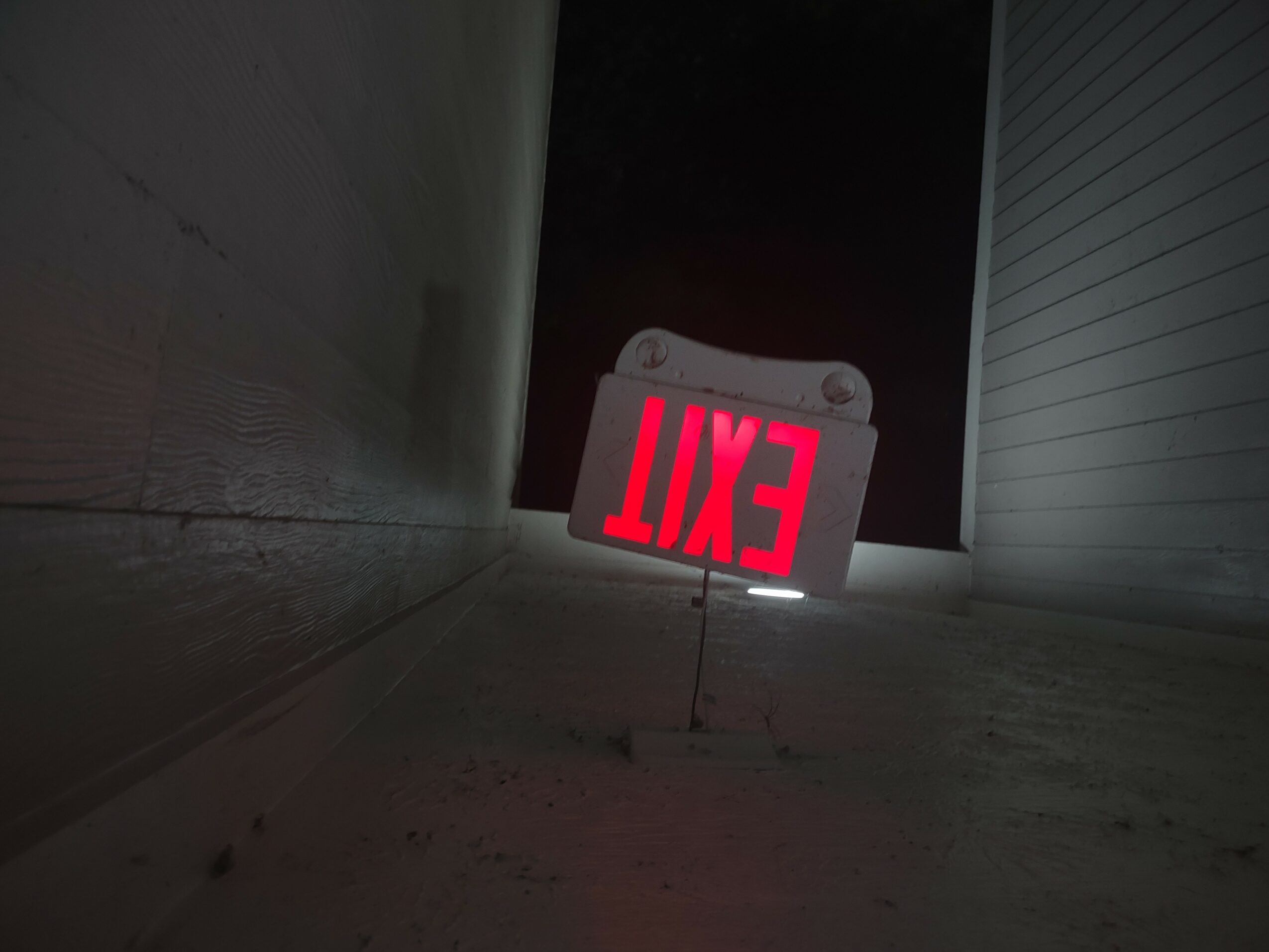 Exit sign on the floor with red letters, viewed from below, in a narrow corridor.