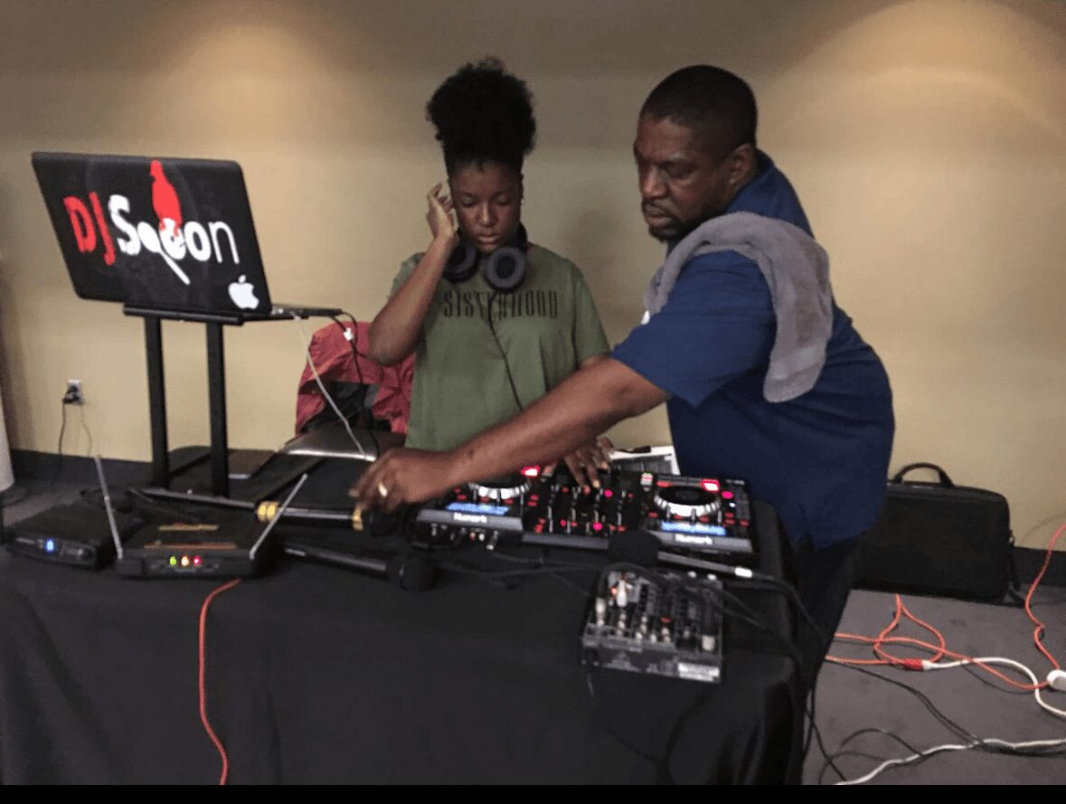 Two people operate DJ equipment with a laptop displaying 'DJ Sason' in a room with beige walls.