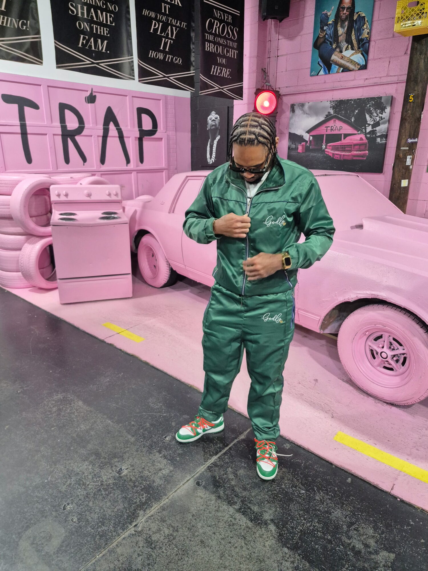Person in green tracksuit standing in front of pink painted cars and wall with graffiti art, indoors.