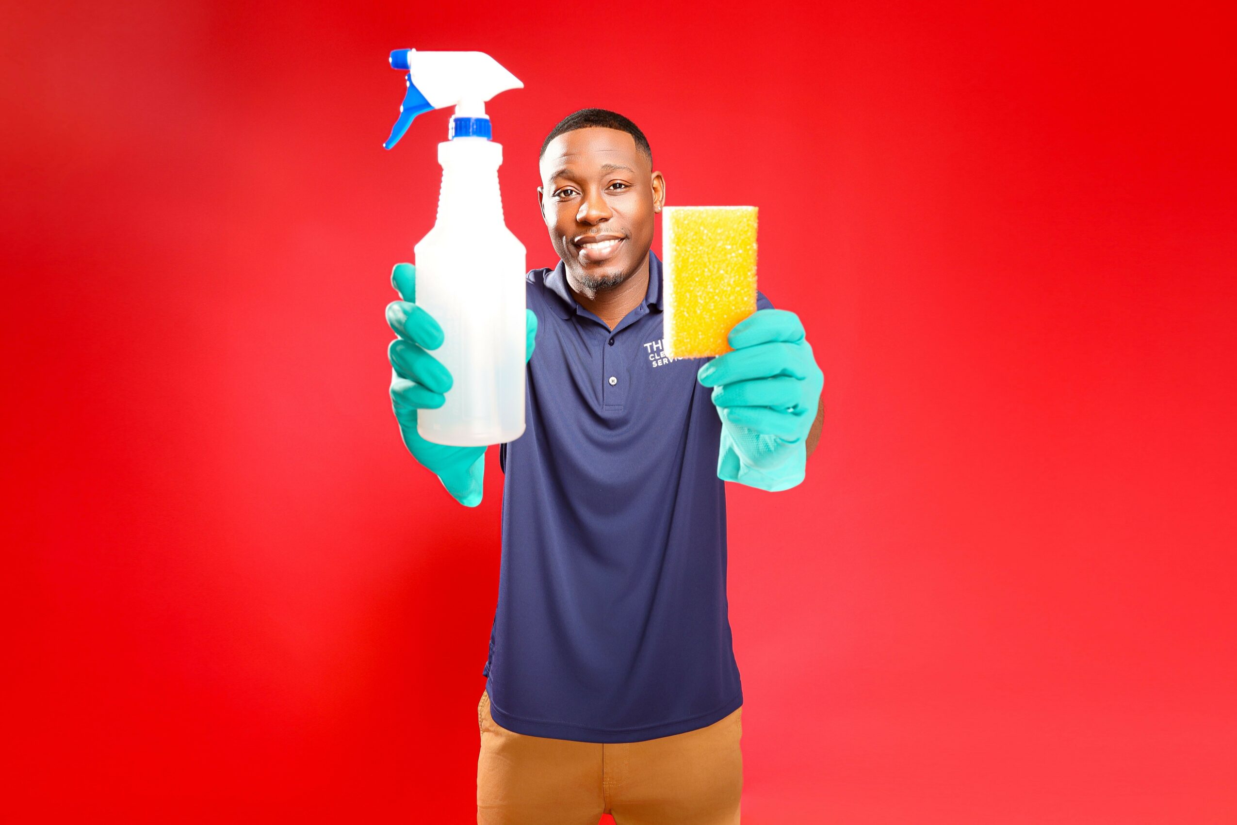 Man holding a spray bottle and sponge, smiling, against a red background.