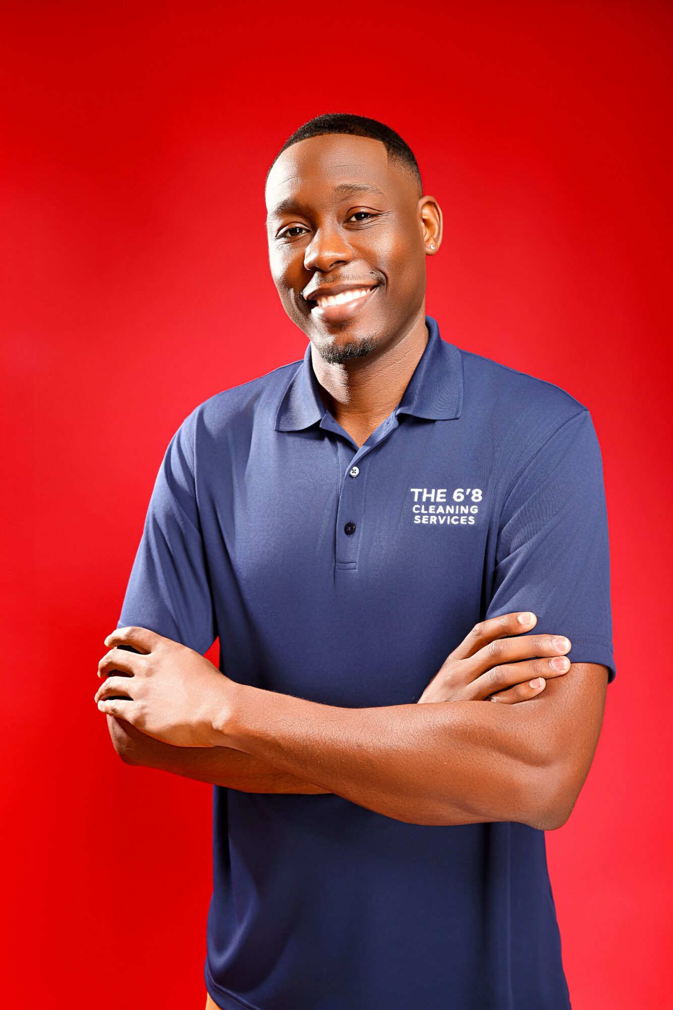 Smiling man with crossed arms wearing a blue polo shirt against a red background.