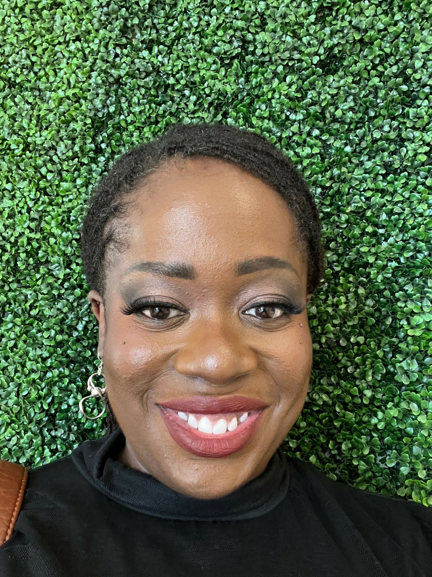 Close-up of smiling woman with dark hair and earrings lying on green foliage background.