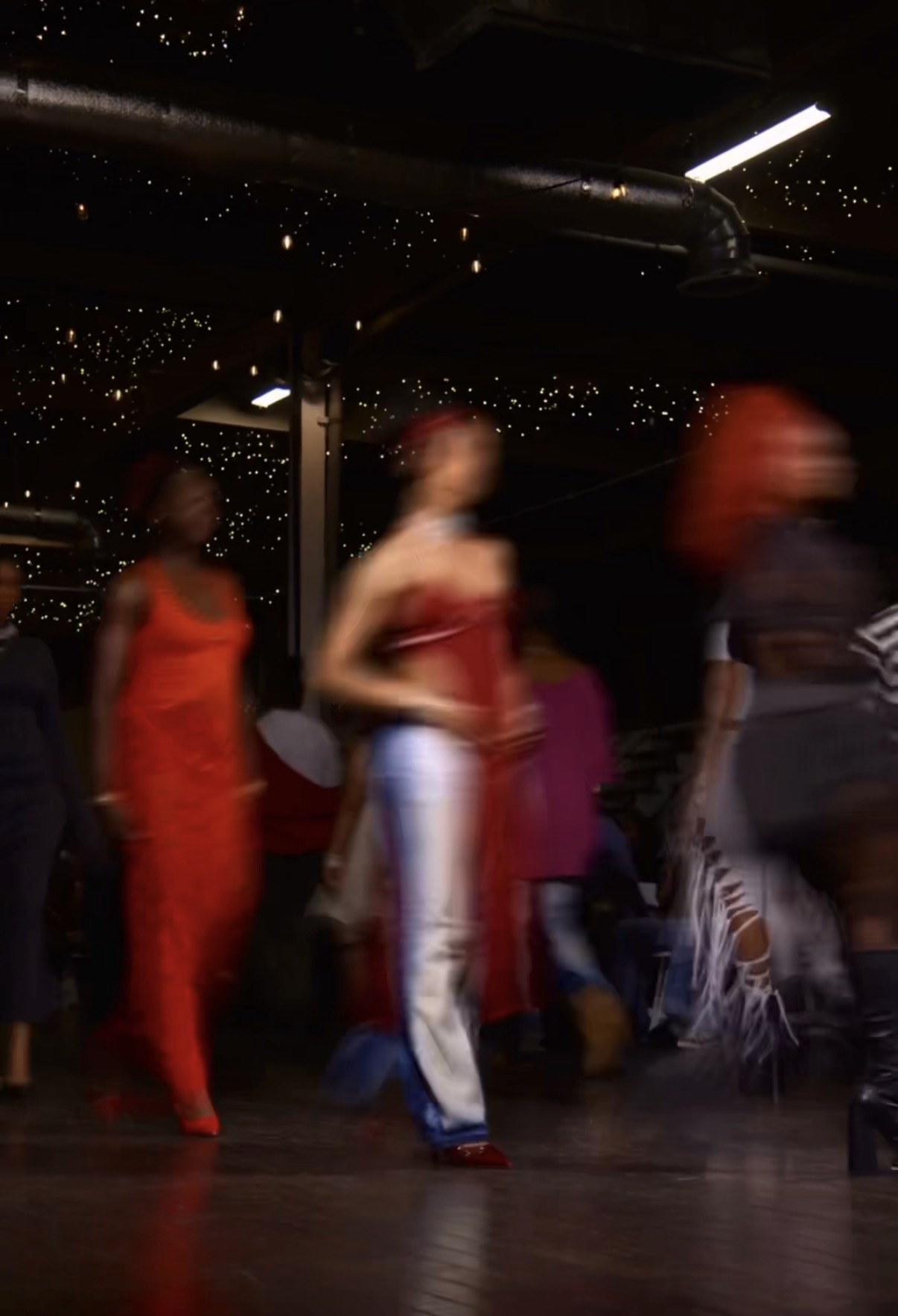 People dancing in a dimly lit venue with star-like ceiling lights, some wearing colorful outfits, blurred motion.