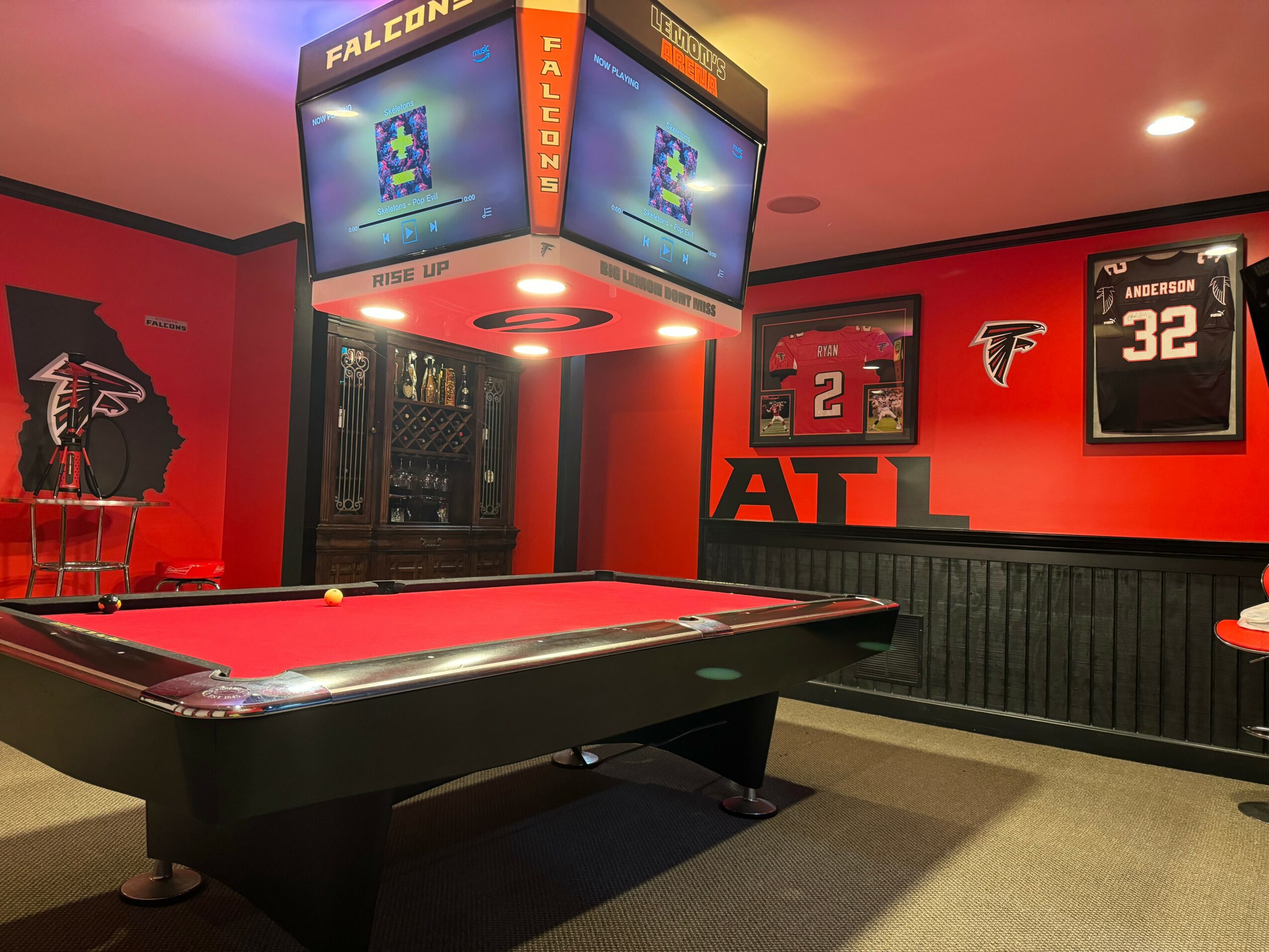 Pool table in sports-themed room with Atlanta Falcons decorations and framed jerseys on red walls.