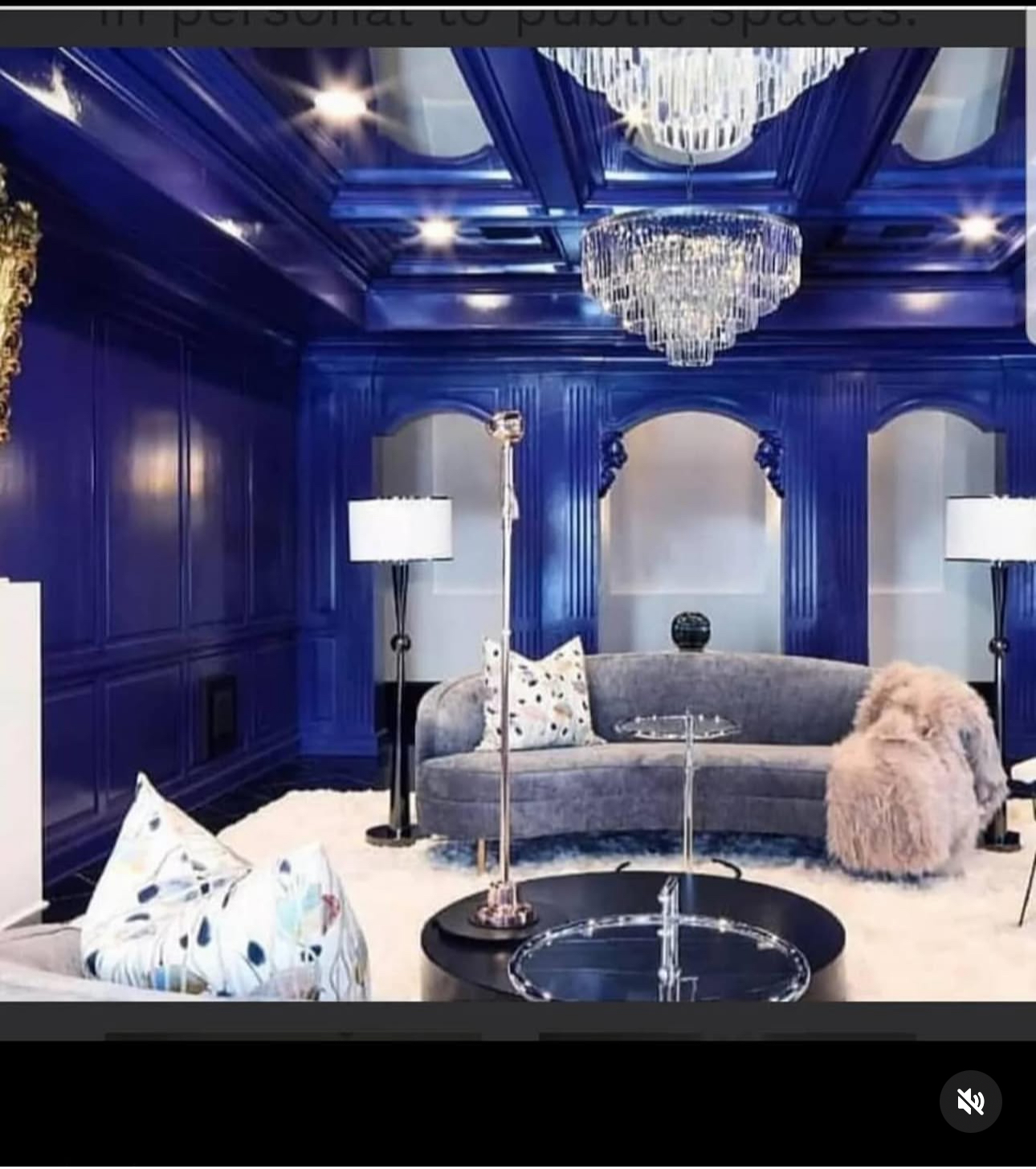 Luxurious room with blue walls, a chandelier, a curved sofa, and two floor lamps, decorated with pillows and a furry throw.