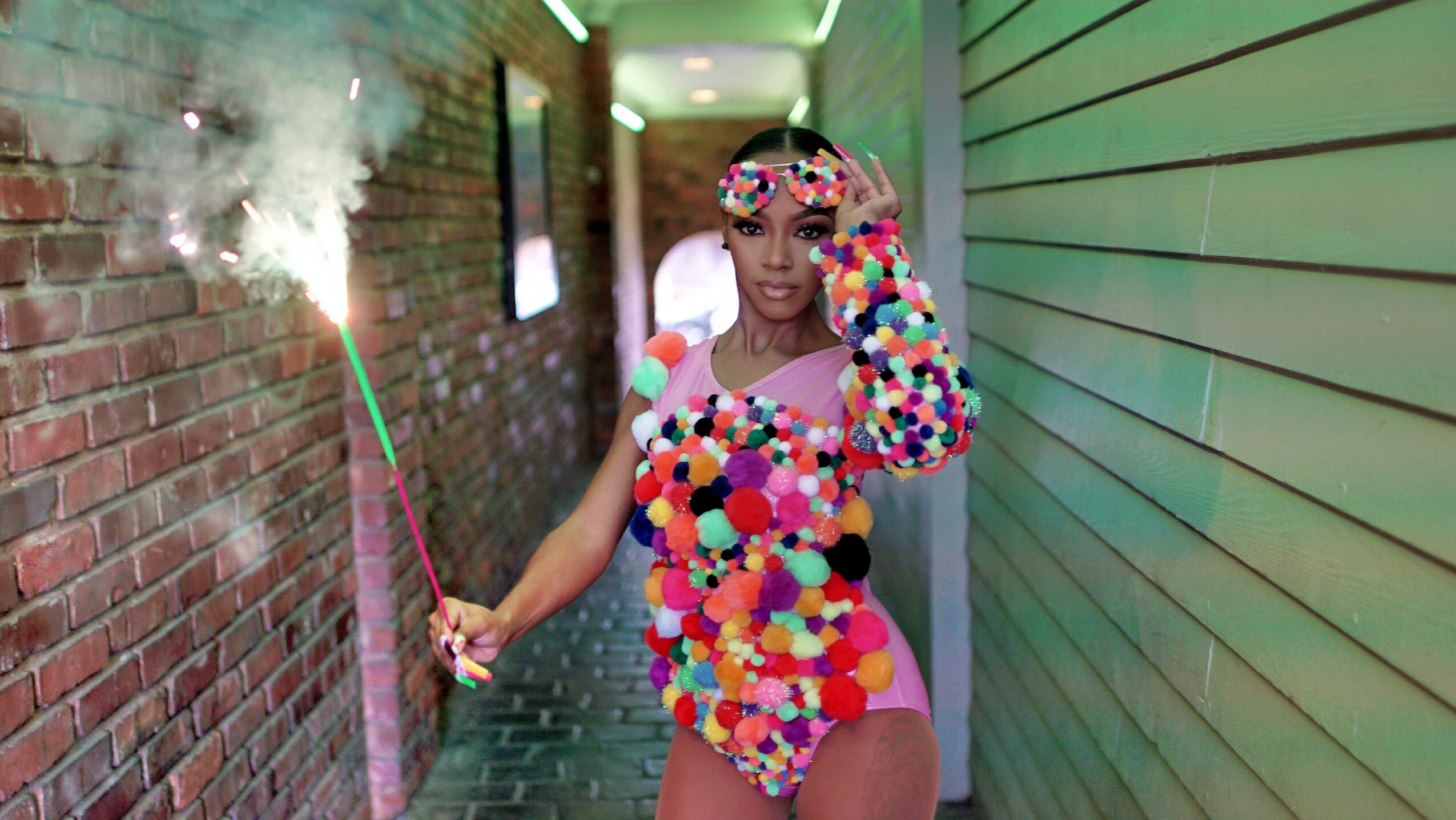 Person in colorful outfit holding a sparkler in a narrow alleyway with brick and wooden walls.