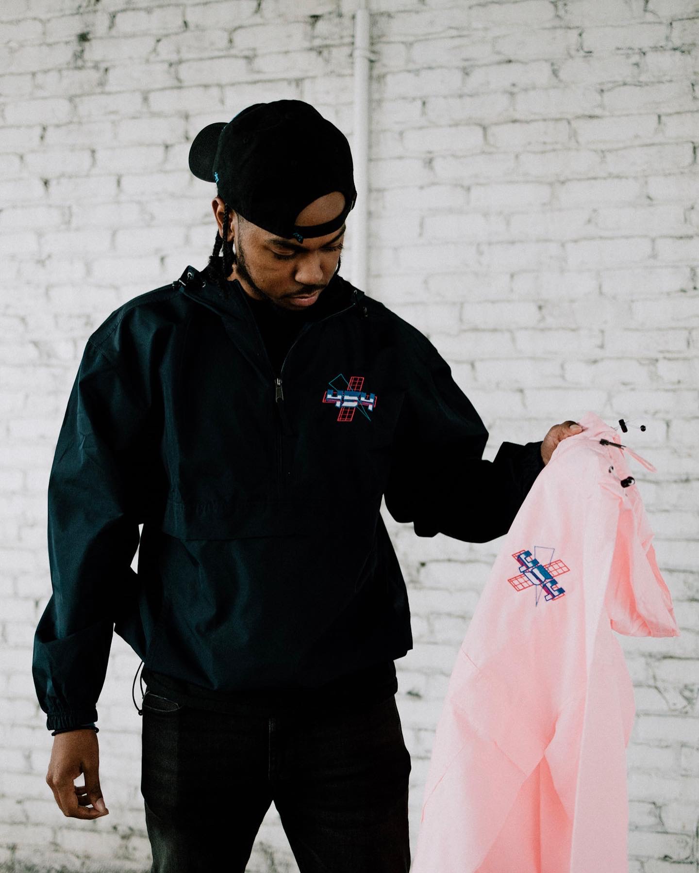Person holding a pink garment with a logo, standing against a white brick wall.
