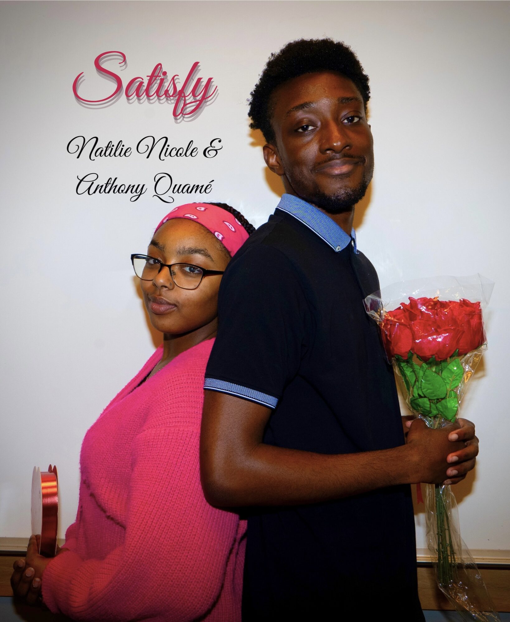 A man holding a bouquet of red roses stands next to a woman with glasses and a pink headband, both smiling.