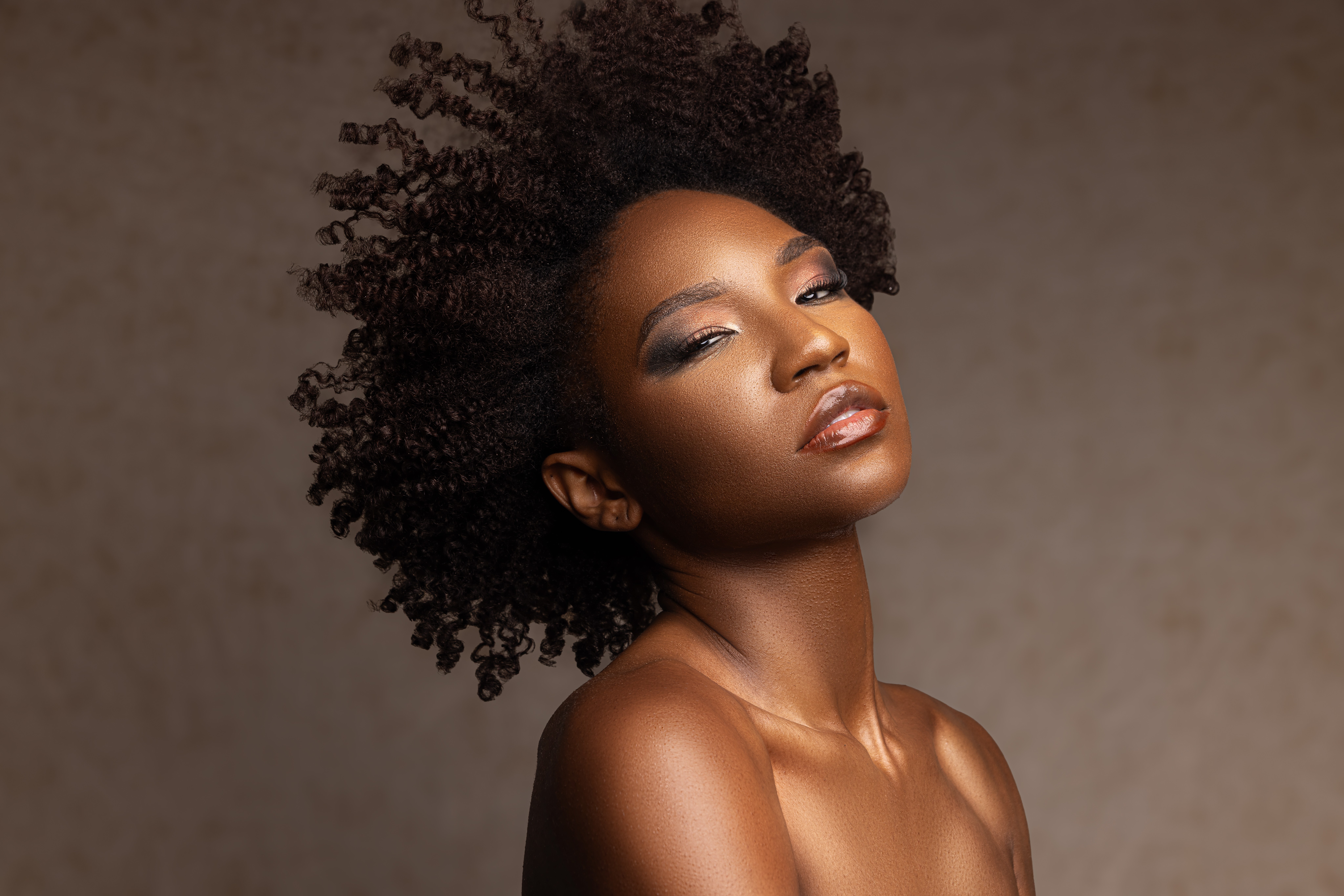 Portrait of a woman with natural curly hair, looking confidently at the camera, against a neutral background.