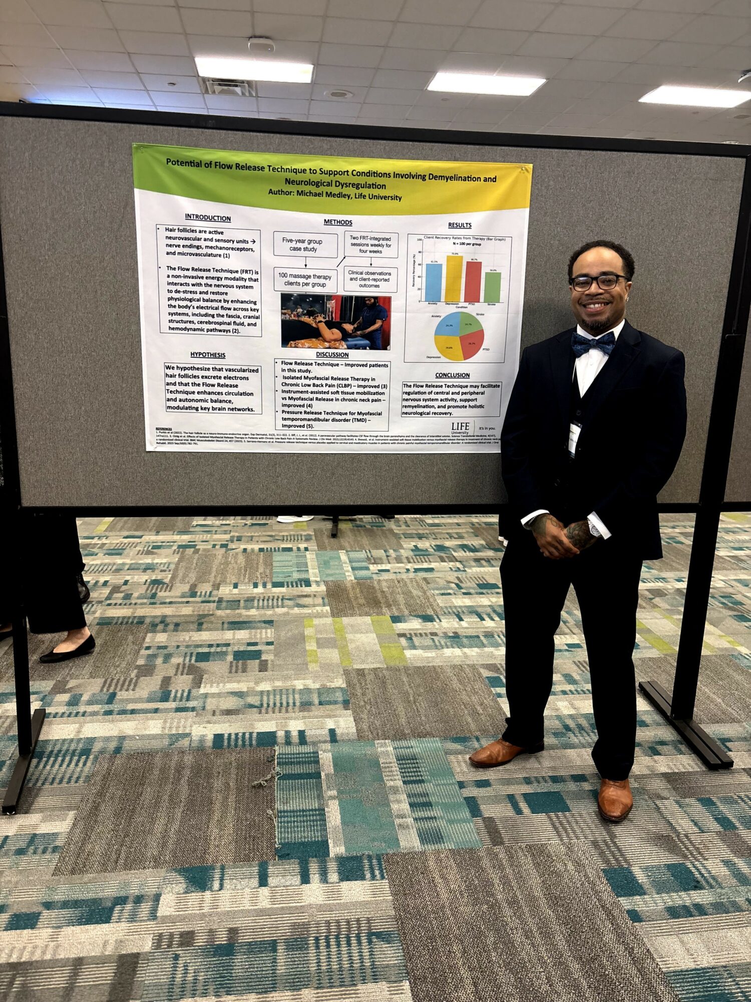 Man in tuxedo standing in front of a presentation board with charts and text, in a conference room.
